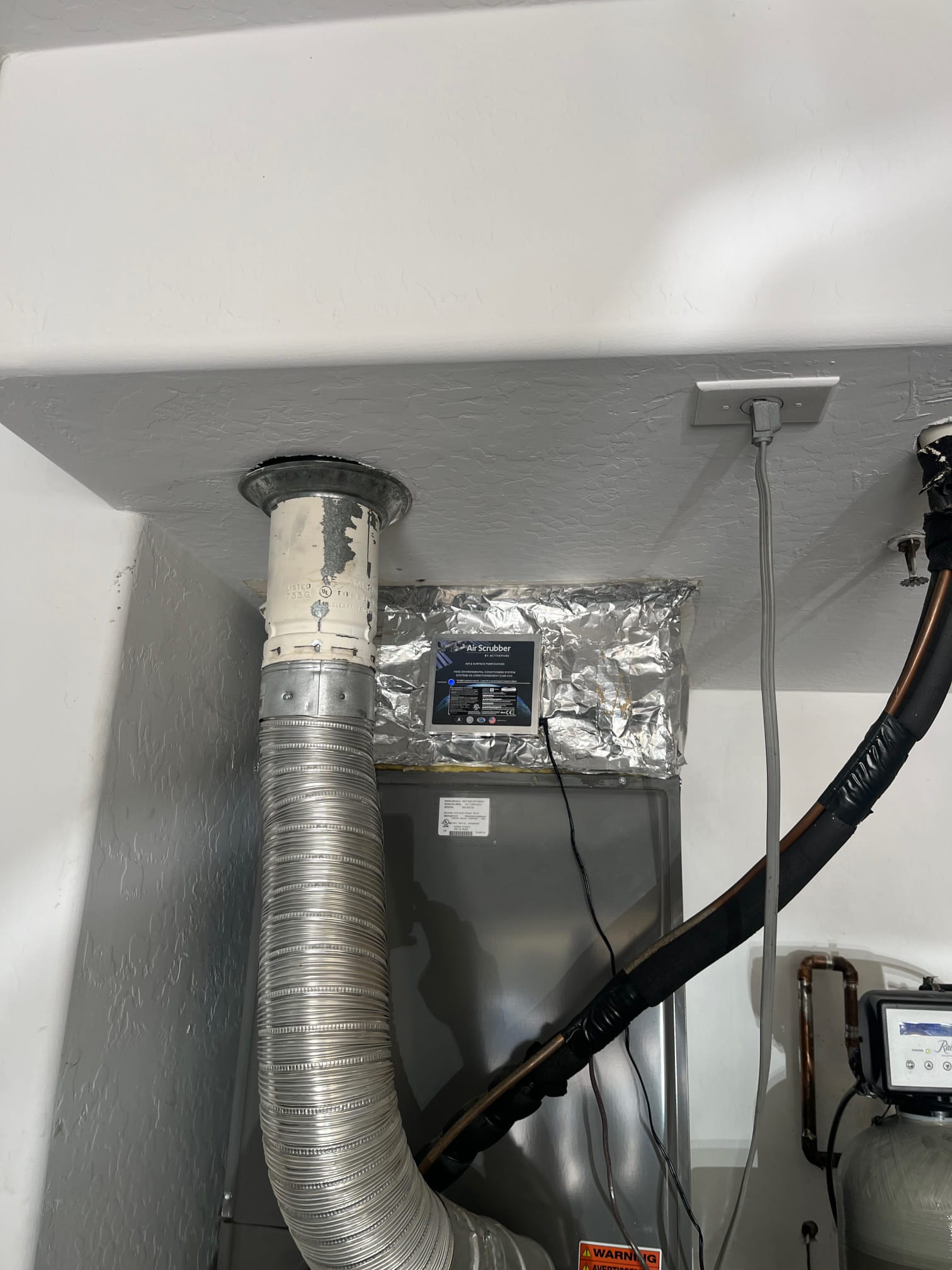 Whole-home air scrubber module installed on the supply plenum above the air handler, with foil tape sealing and flex duct connected.