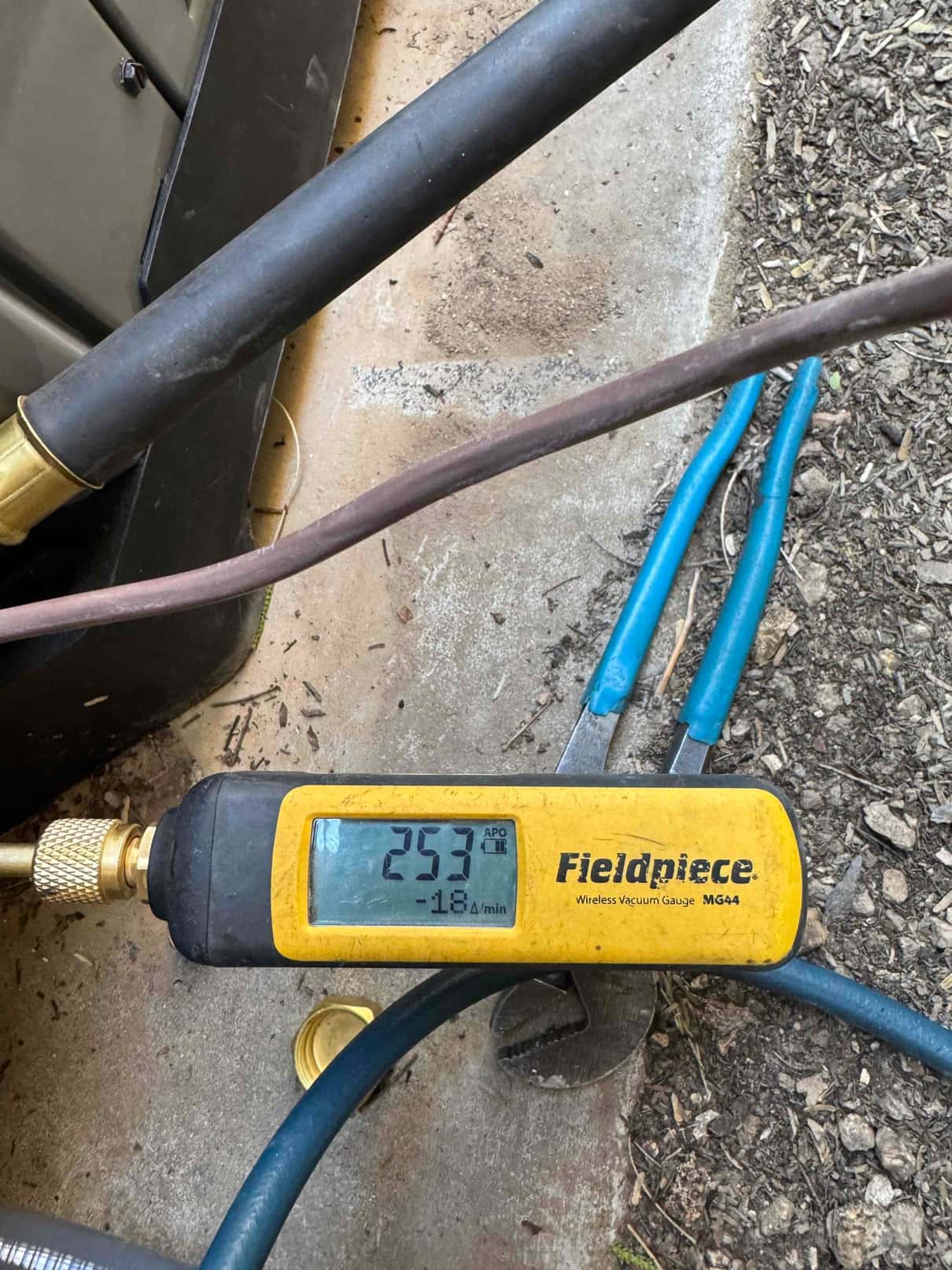 Wireless vacuum gauge connected at the condenser shows 253 microns during system evacuation, confirming a deep vacuum before charging.
