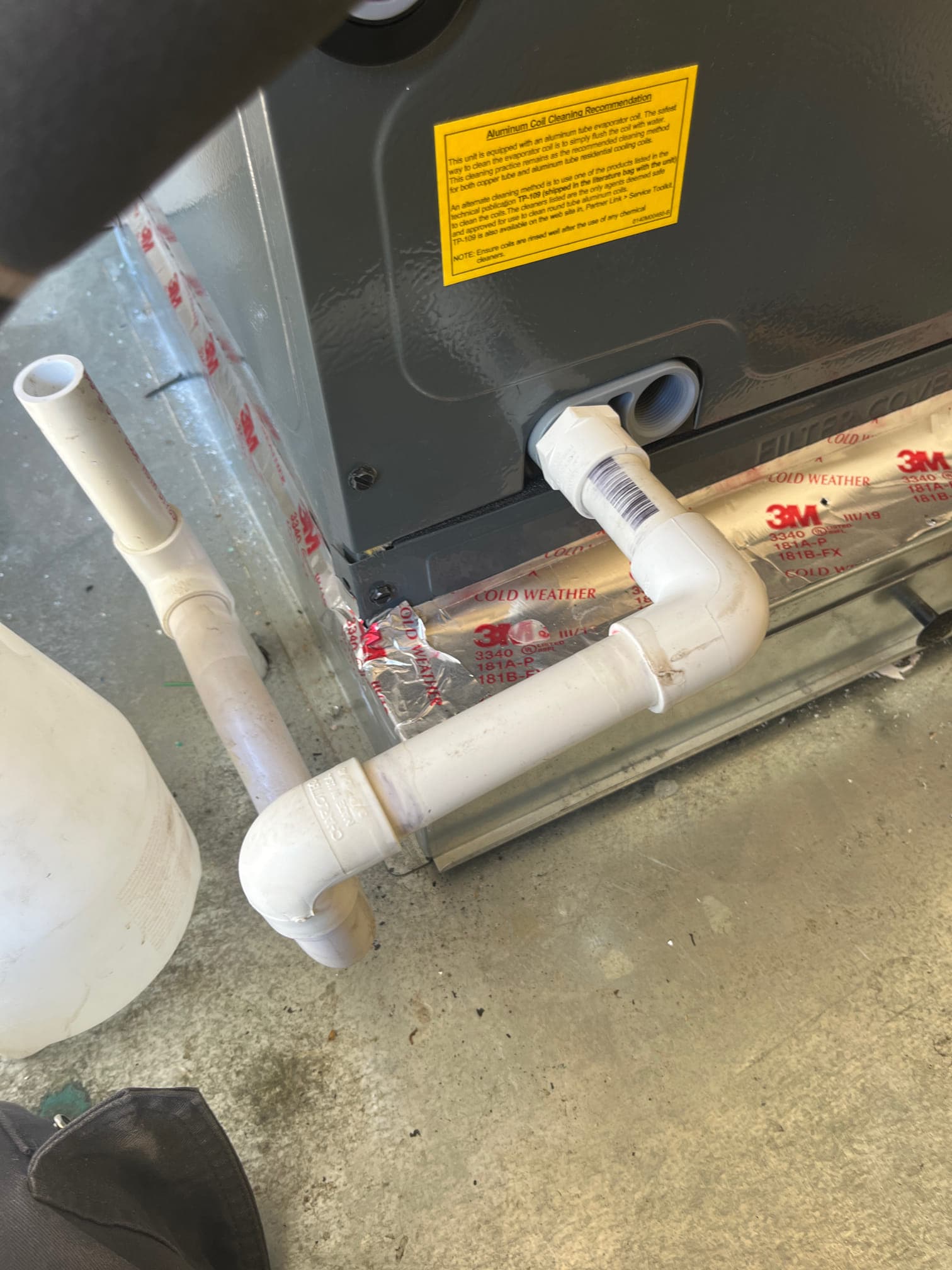 Air handler condensate drain assembly with PVC trap and cleanout installed, sealed to the unit with foil HVAC tape.