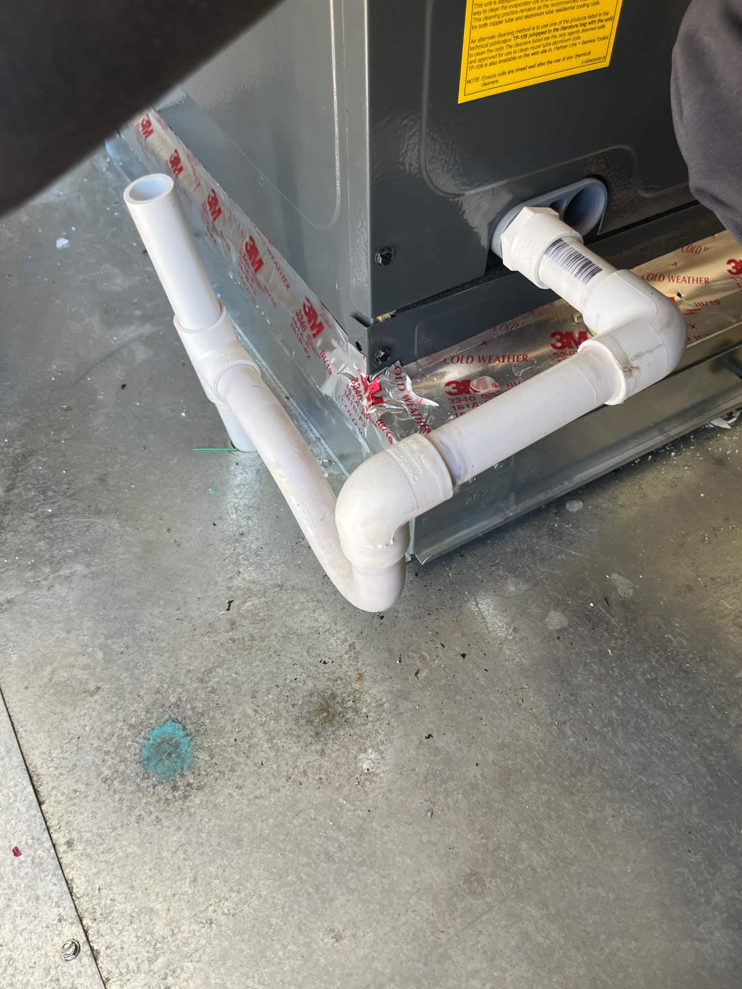 Air handler condensate drain assembly with PVC trap and cleanout installed, sealed to the base with foil HVAC tape.