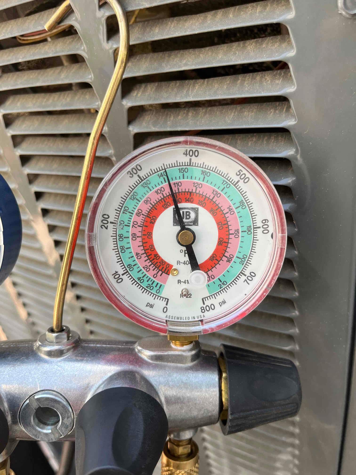 Analog refrigerant manifold gauge connected at the outdoor unit, low-side needle indicating suction pressure during system operation.
