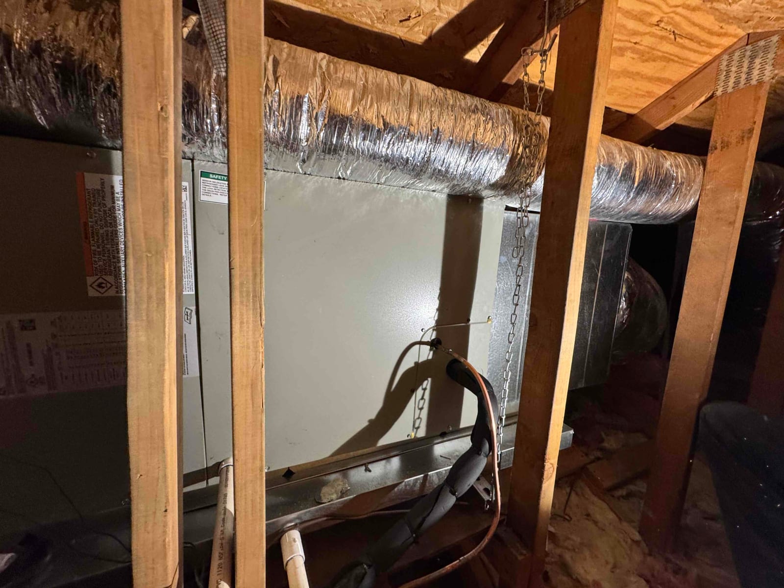 Air handler installed in attic with insulated supply and return ducts connected and condensate drain piping visible.