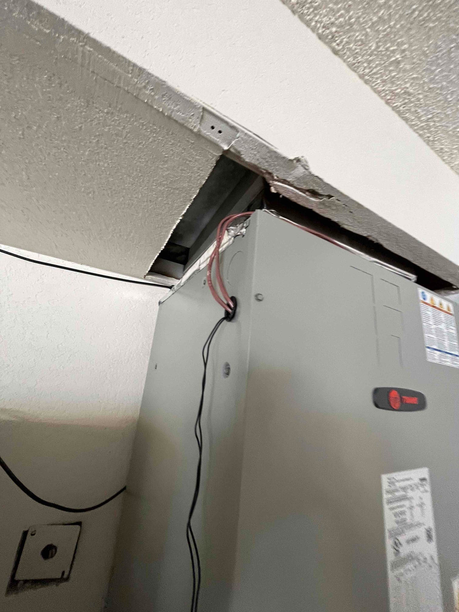 Air handler installed in a closet with exposed wiring and an open ceiling access panel above the unit.