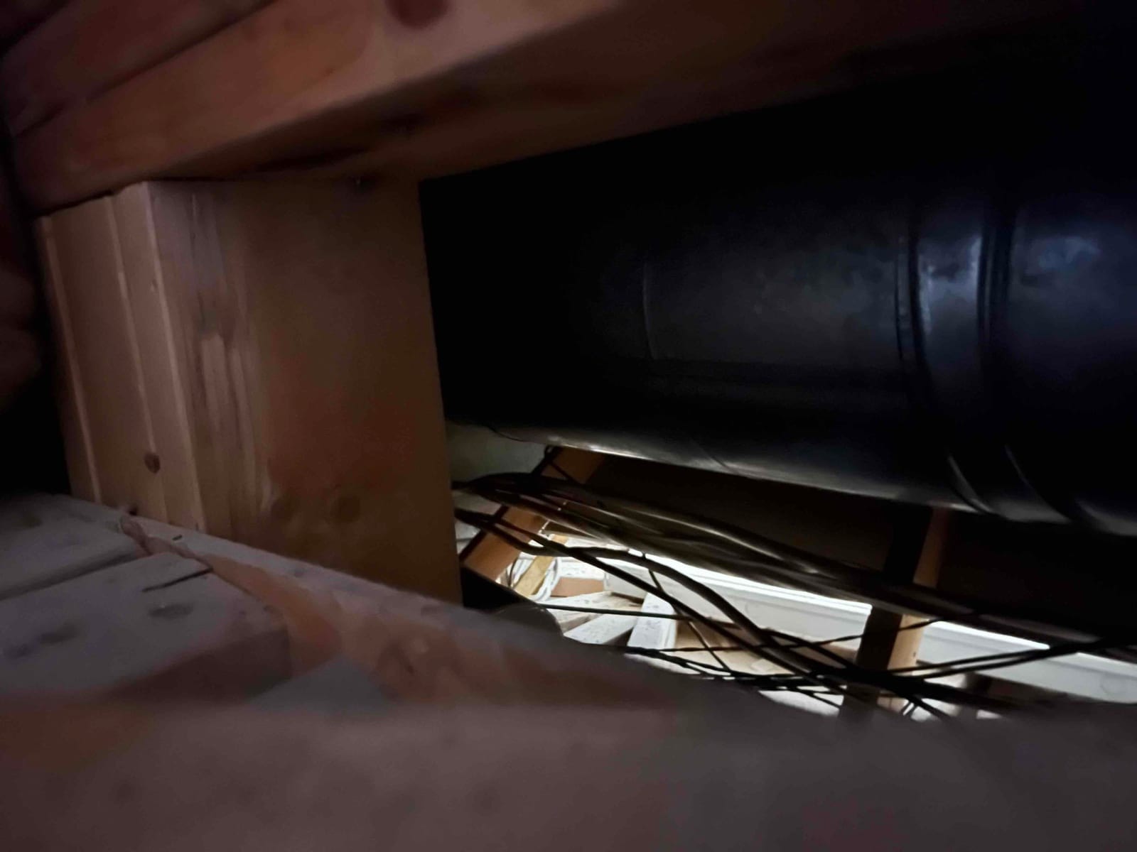 Attic view showing a round metal duct run passing through framing, with wiring visible along the joists.