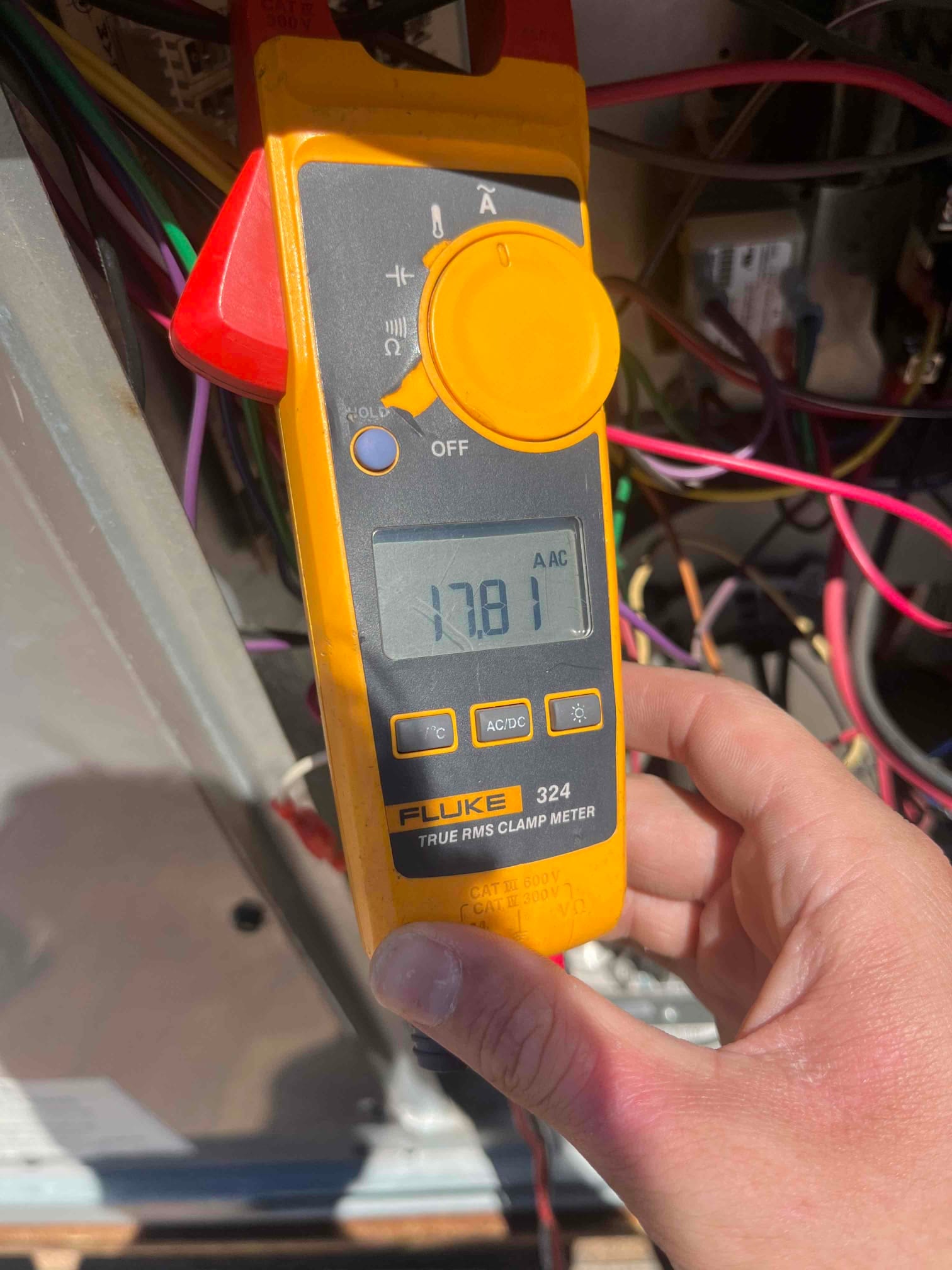 Clamp meter displays 17.81 A AC on a single conductor inside the condenser control compartment during testing.