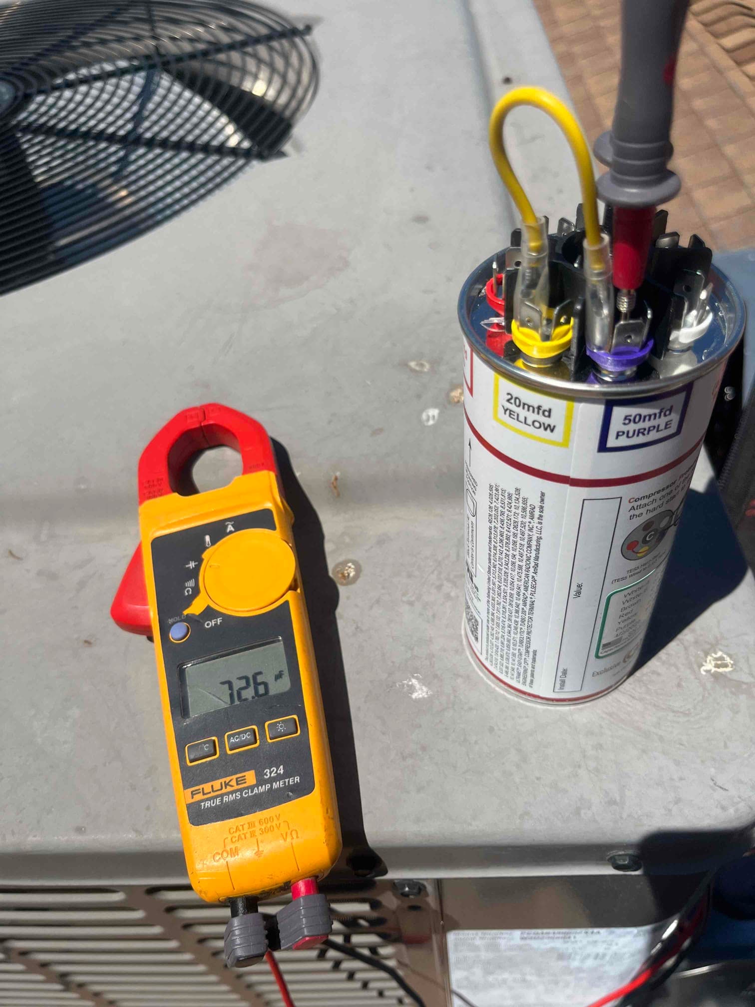 Clamp meter displays 7.26 A while measuring current on a conductor next to a dual run capacitor rated 20/5 μF.