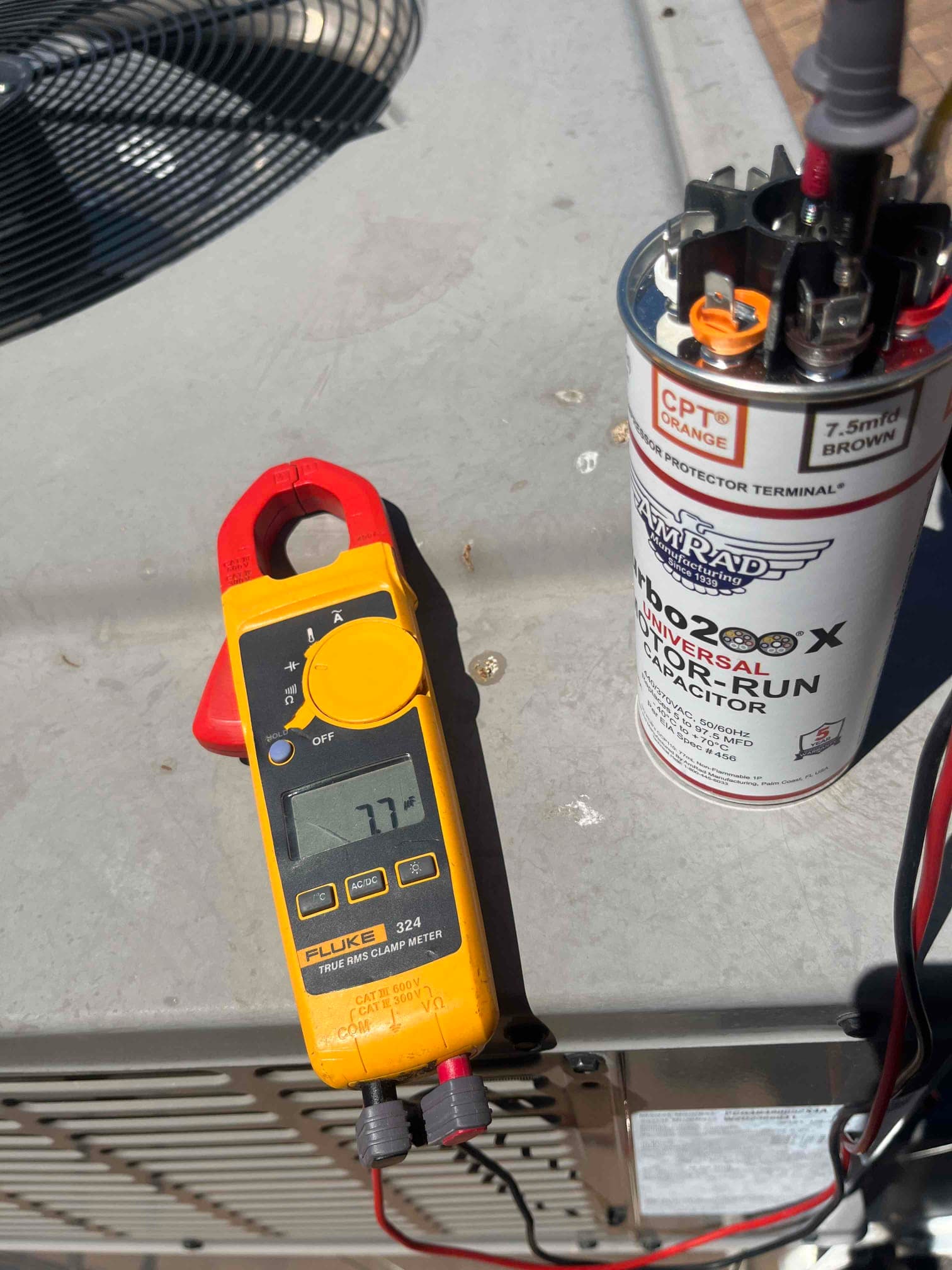 Clamp meter displays 7.7 A while measuring current on a conductor next to the installed run capacitor.
