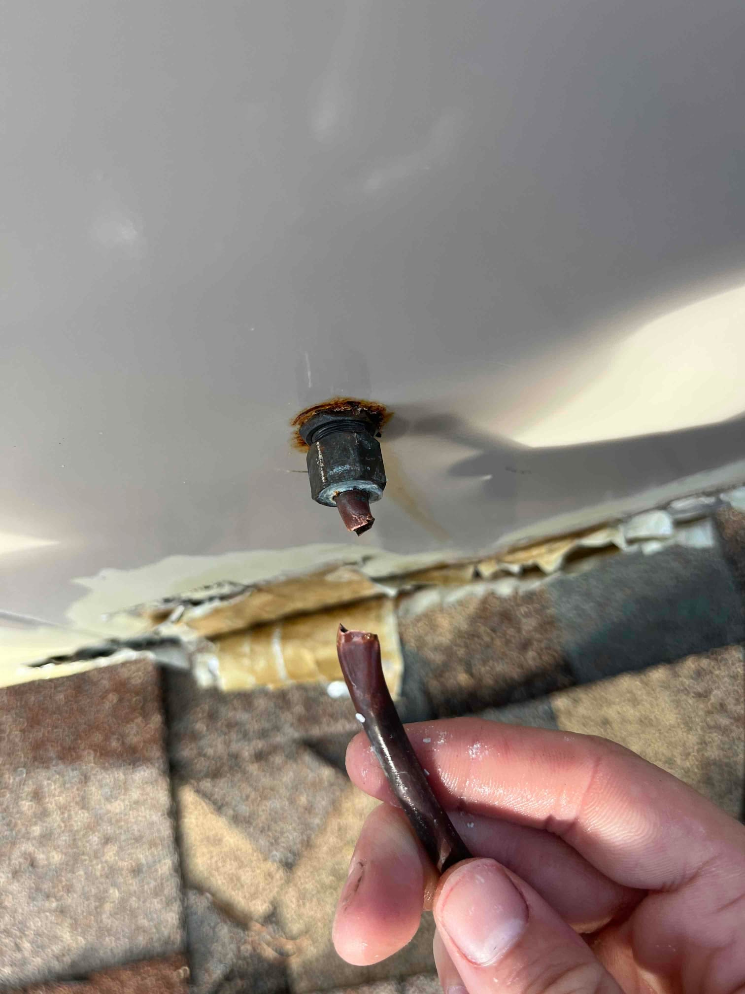 Close-up of a broken brown tubing connection at a rusted fitting on HVAC equipment, with the detached end held for reference.