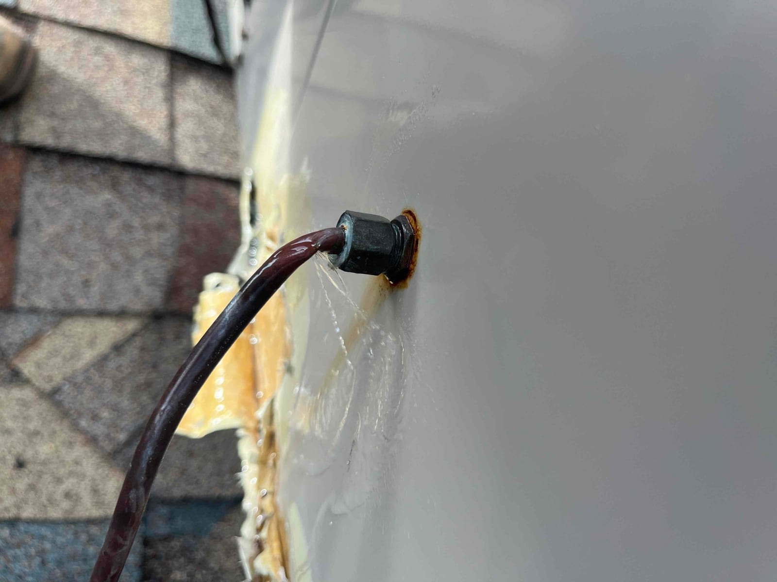 Close-up of a brown wire entering an HVAC cabinet through a rubber grommet, with rust and sealant around the penetration.