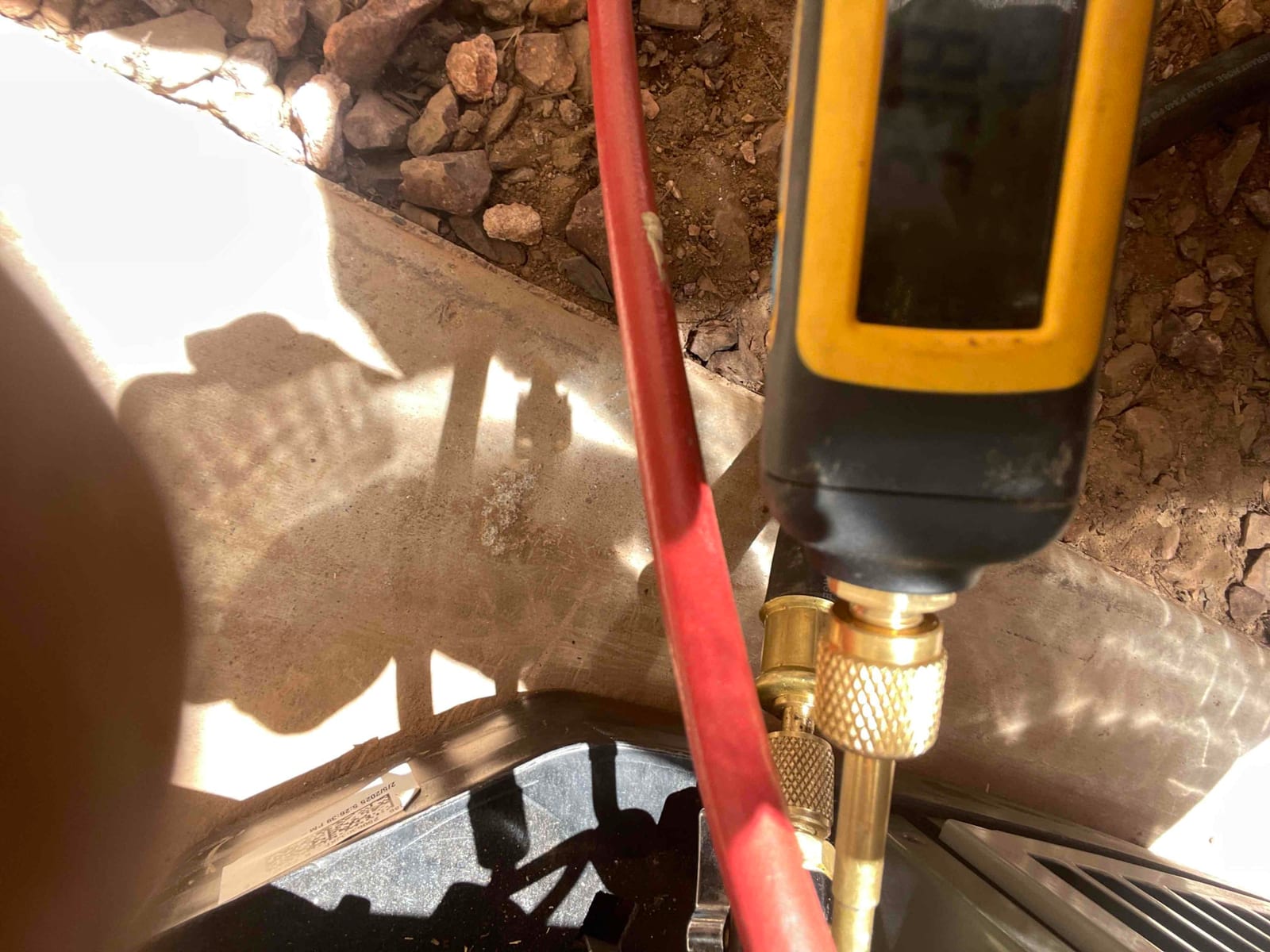 Close-up of a service hose connected to a brass fitting at the outdoor unit during HVAC work.