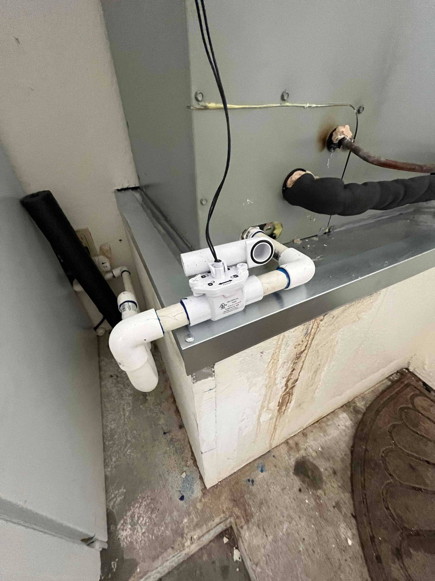 Condensate drain assembly with float safety switch installed at the air handler, connected to insulated refrigerant lines and metal drain pan.