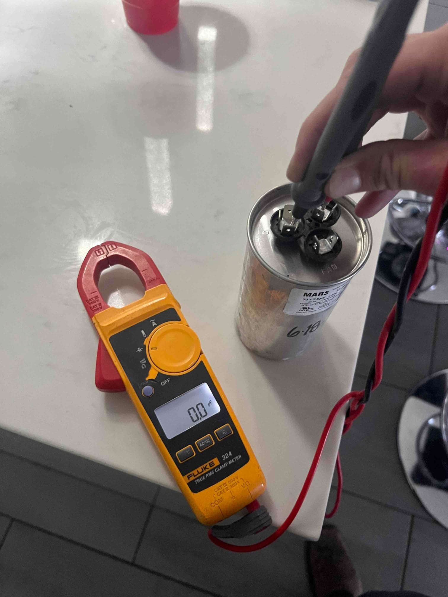 Digital multimeter set to capacitance shows 0.0 μF while probing terminals on a metal can run capacitor.