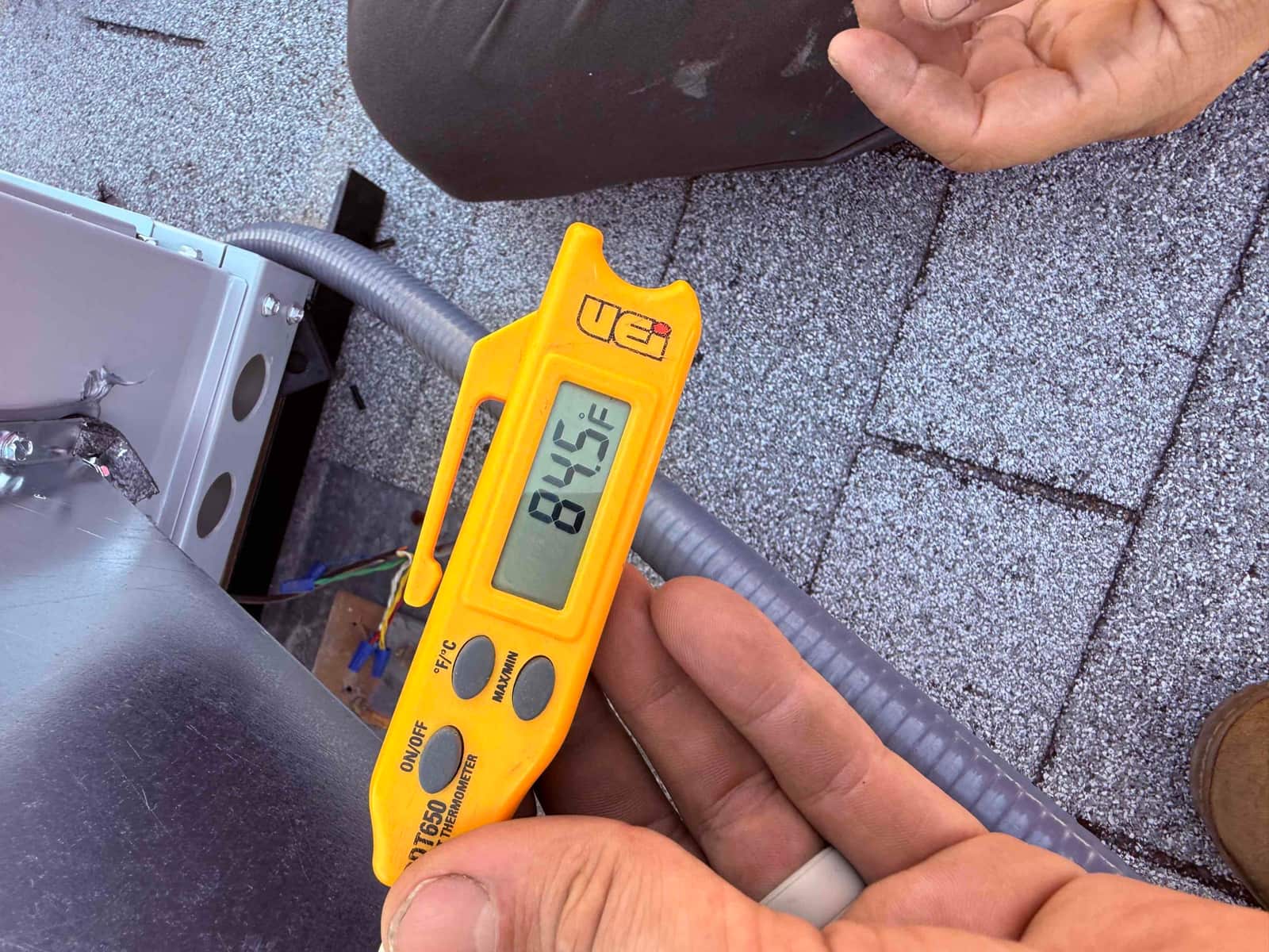 Digital thermometer displays 84.5°F while checking air temperature near the rooftop HVAC installation.