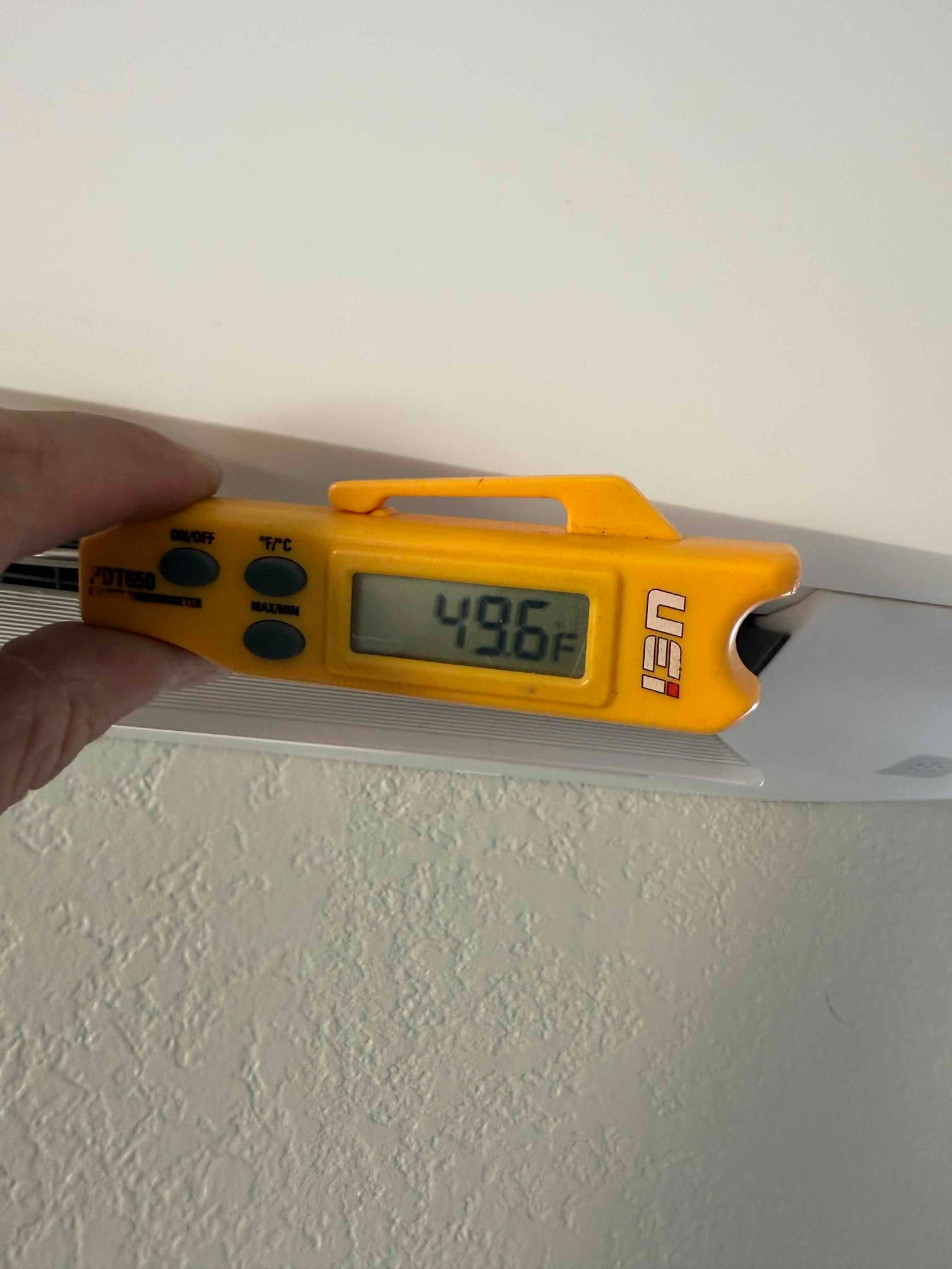 Digital thermometer at the indoor mini-split discharge grille reads 49.6°F, documenting cold supply air during cooling operation.