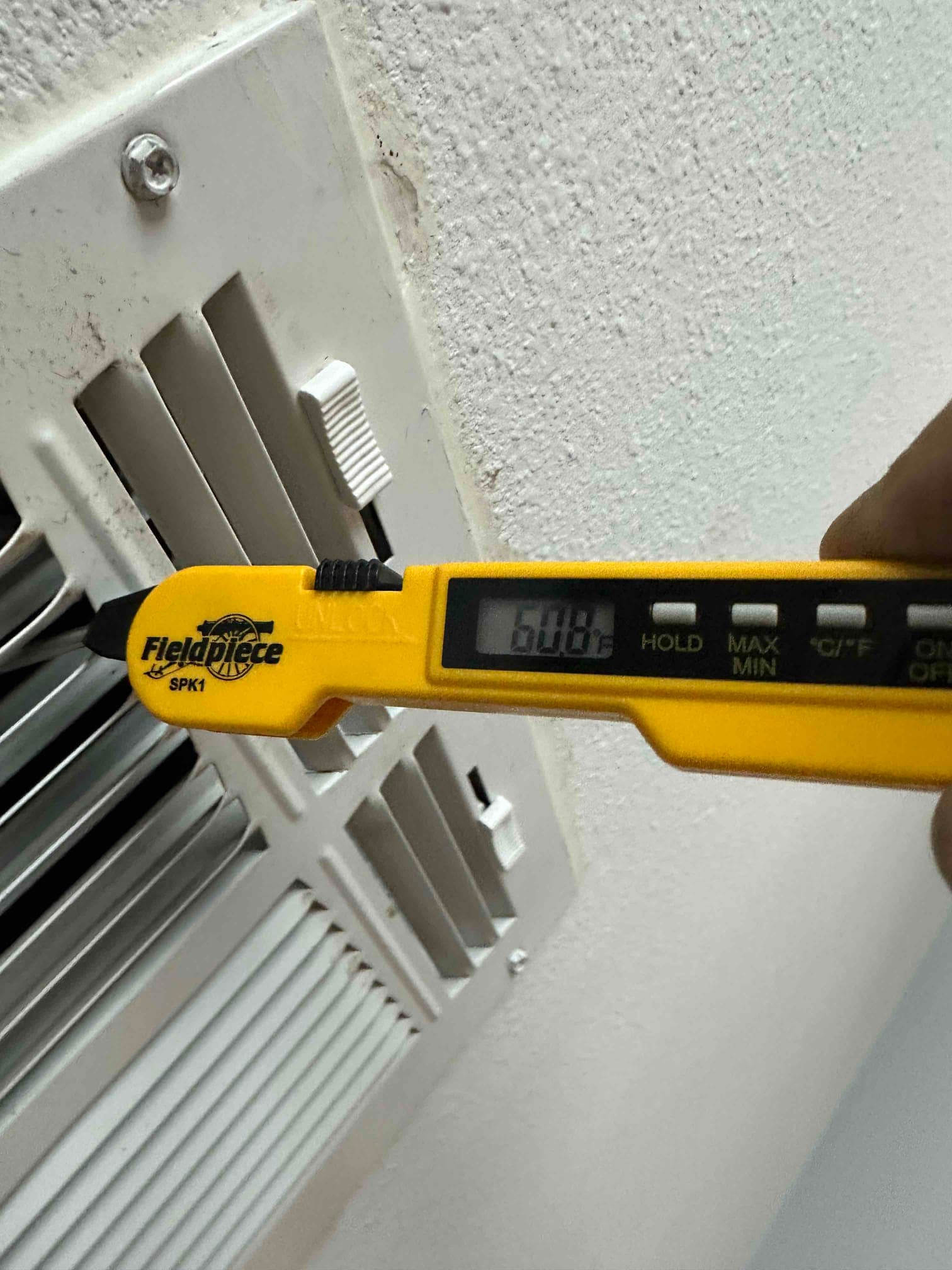 Digital thermometer inserted at a supply register reads 60.8 degrees Fahrenheit, documenting cooled air temperature leaving the system.