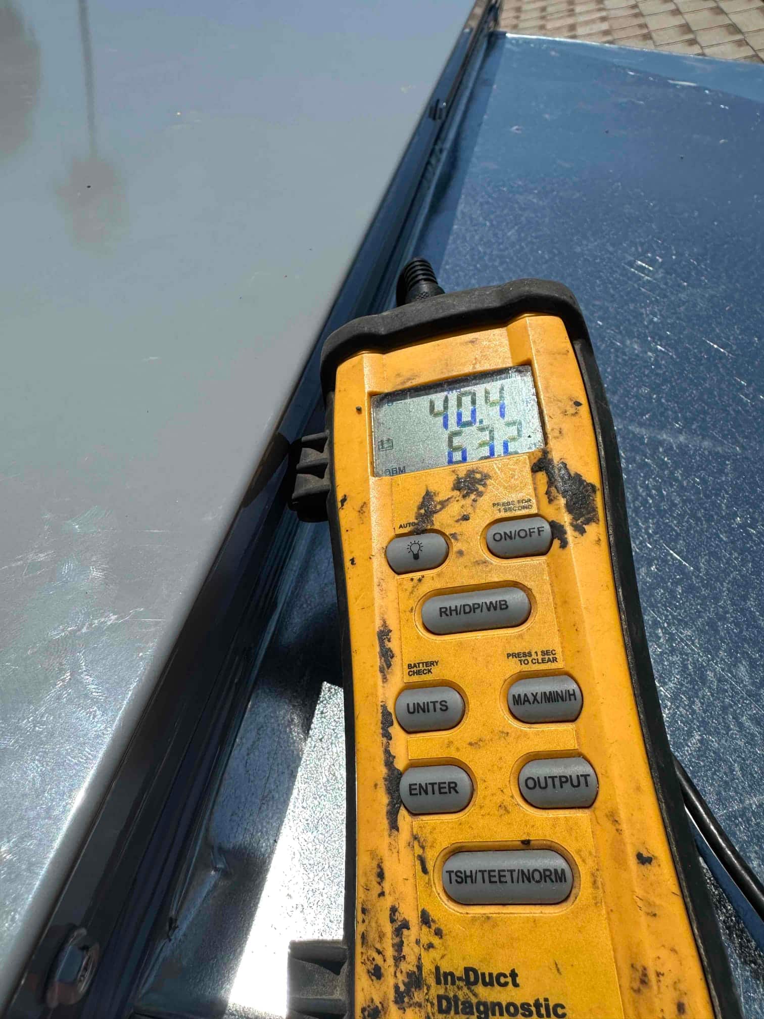 Digital thermometer probe in use shows 40.4 degrees and 63.7 degrees during air temperature measurements on the HVAC system.