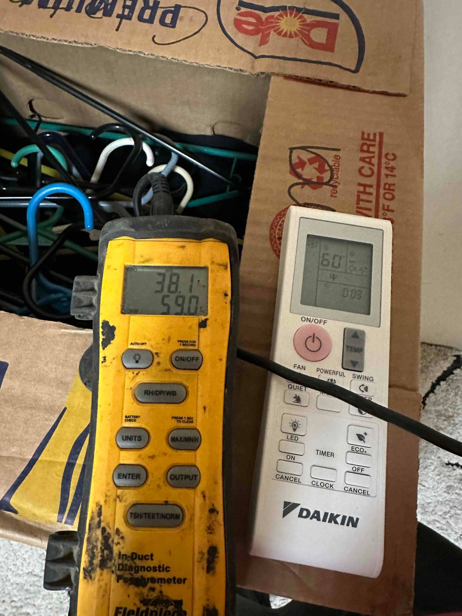 Digital thermometer shows 59.0 degrees Fahrenheit, documenting supply air temperature during commissioning alongside a remote control.