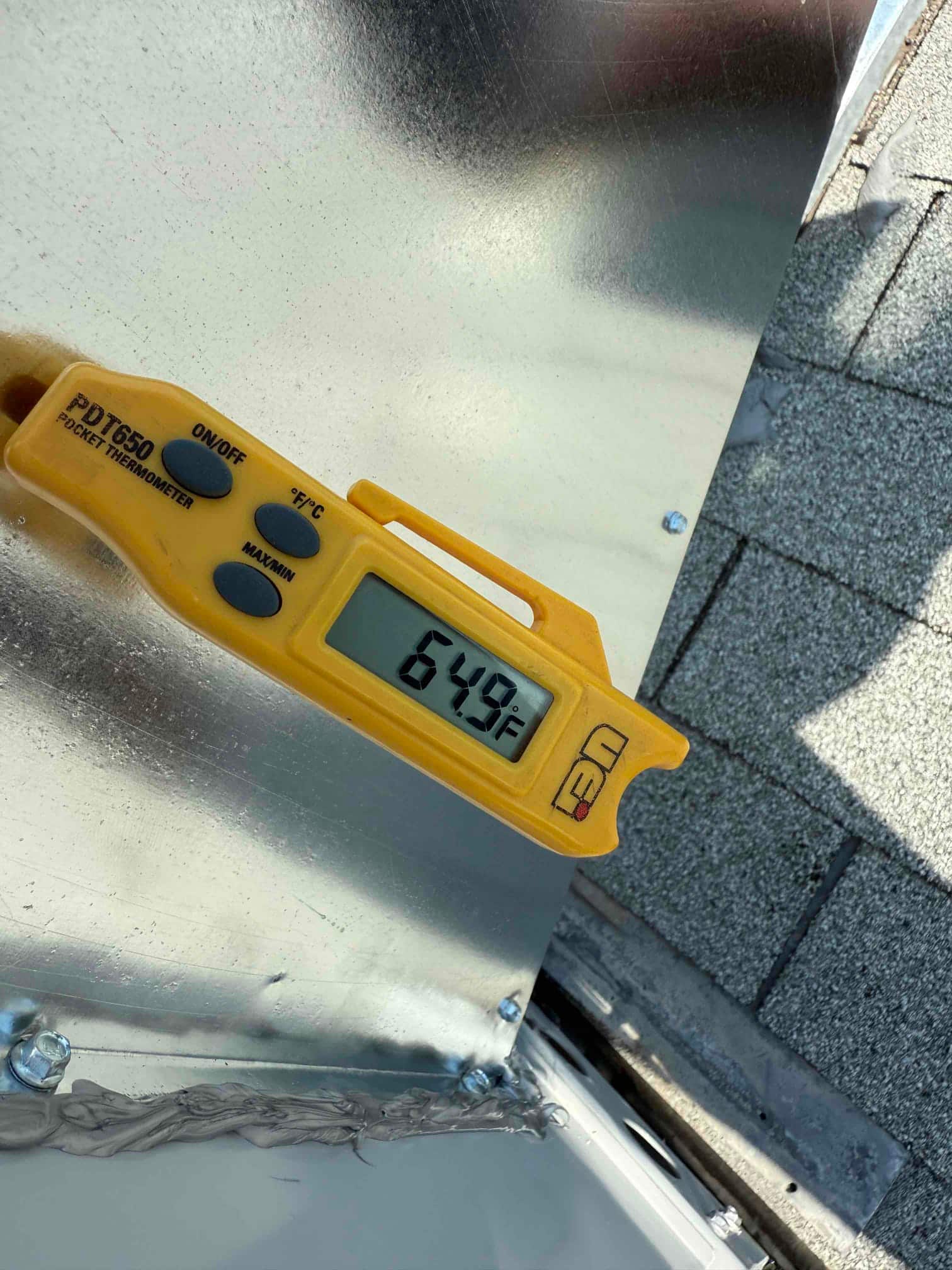 Digital thermometer shows 64.9°F while checking air temperature at the HVAC installation site.
