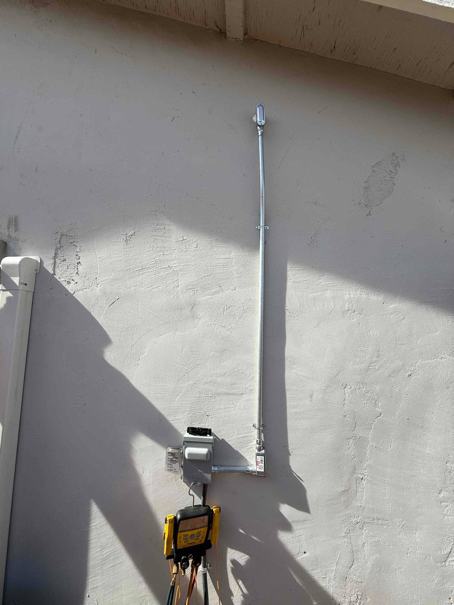 Exterior disconnect and rigid conduit installed on stucco wall with digital manifold hanging below during mini-split installation.