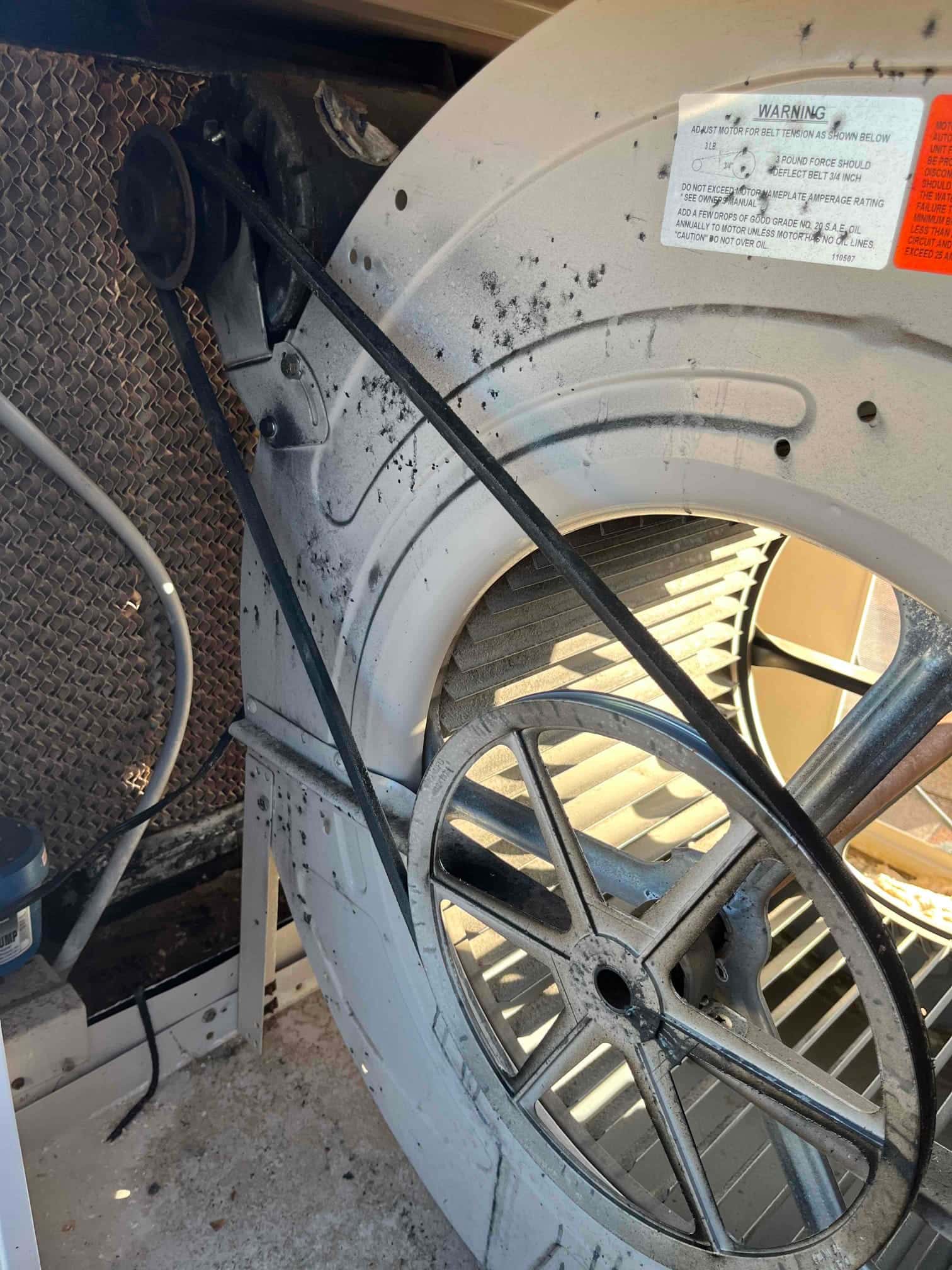 Indoor blower assembly with belt drive exposed, showing worn belt dust on the housing and aligned pulleys.