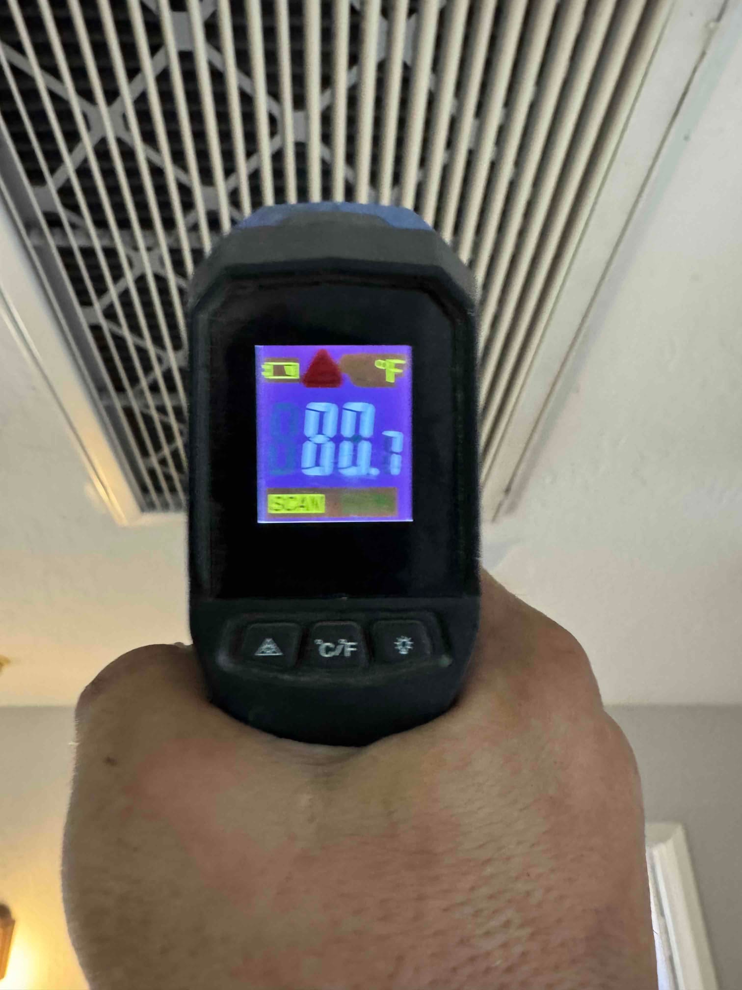 Infrared thermometer aimed at a return grille shows 80.7 degrees Fahrenheit during airside commissioning.