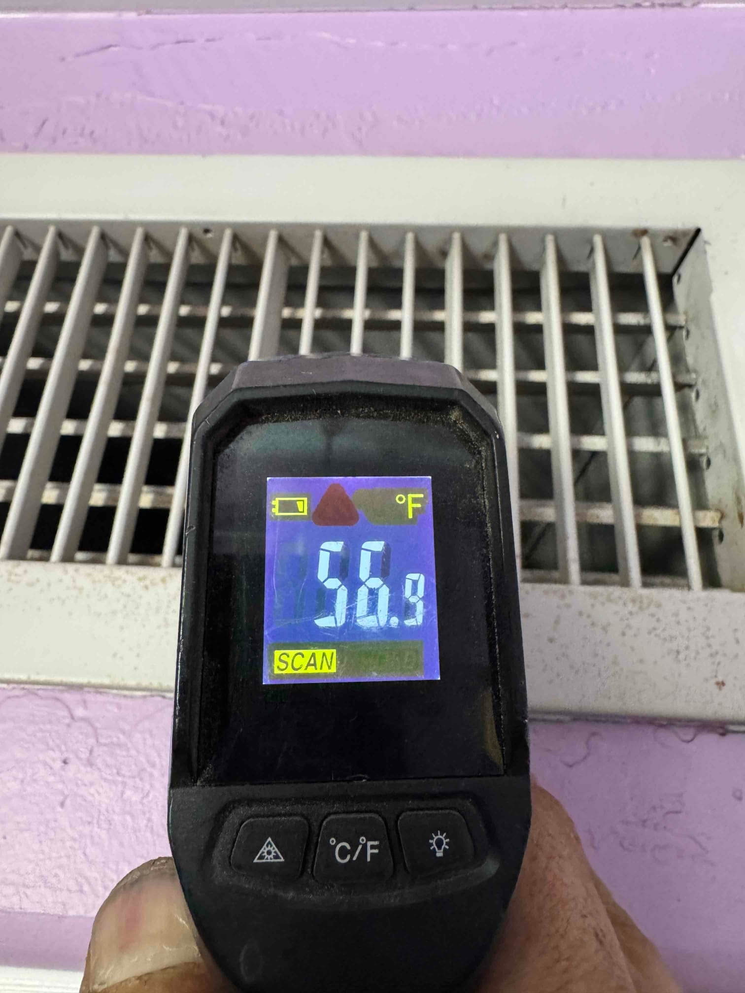 Infrared thermometer measures 56.9°F at a supply register, documenting cooled air temperature leaving the system.