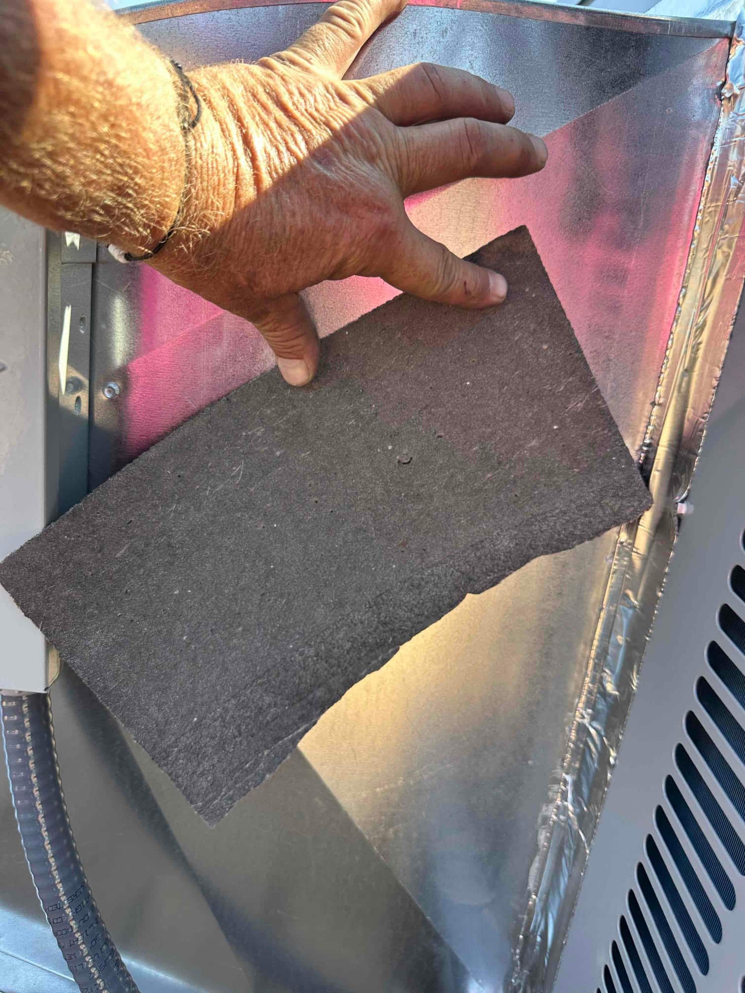 Installer places sheet-metal transition and insulation at the package unit discharge, showing sealed duct connection and flexible conduit nearby.