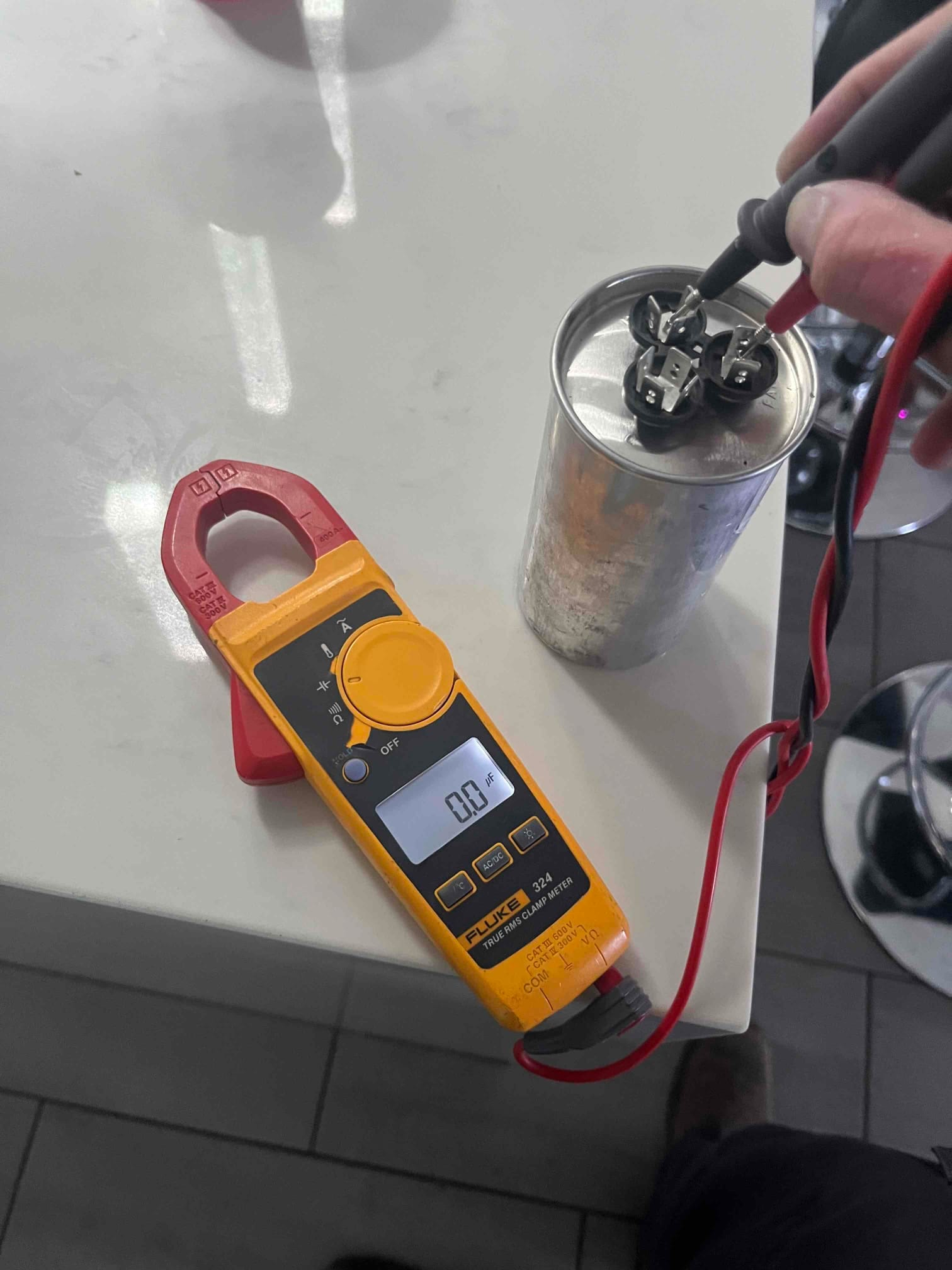 Multimeter set to capacitance measures the dual-run capacitor terminals, displaying 0.0 μF on the screen.
