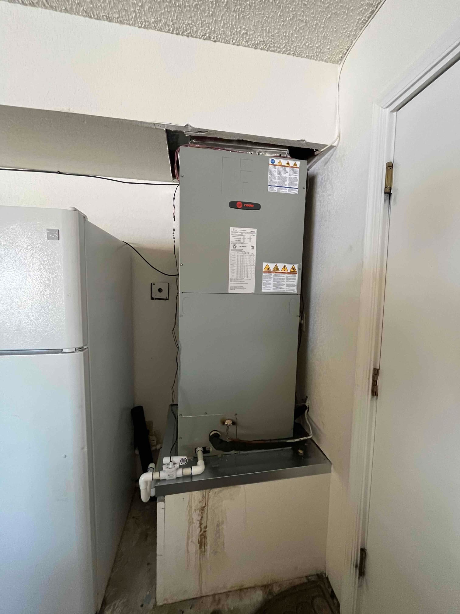 New air handler installed in closet with insulated refrigerant lines and PVC condensate drain assembly connected to the primary pan.