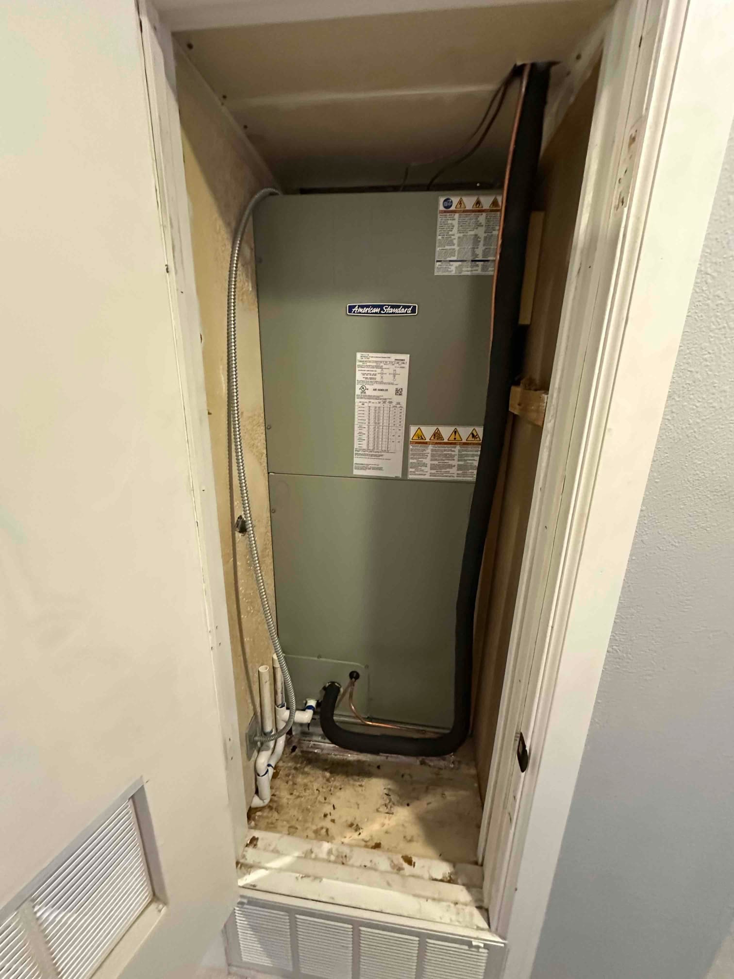 New air handler installed in a closet with insulated refrigerant line, condensate piping, and flexible electrical conduit connected.