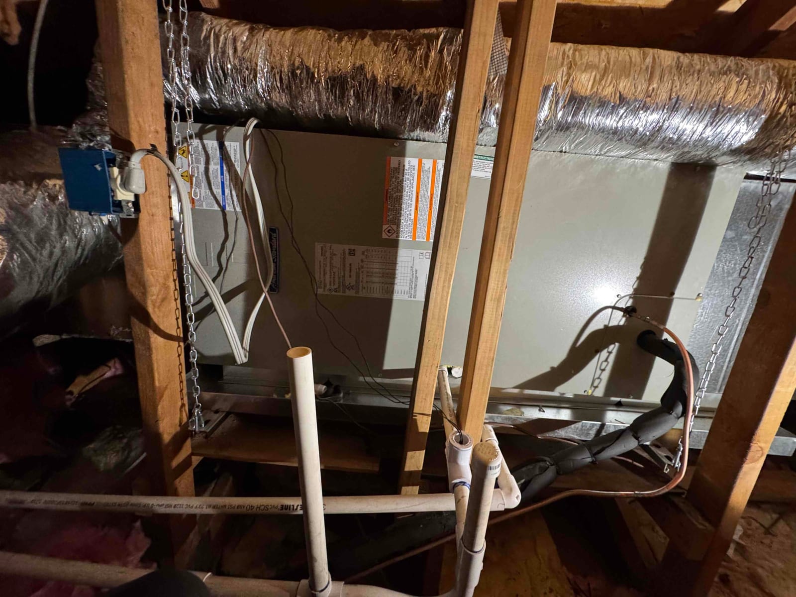 New air handler suspended in the attic with insulated supply and return ducts, condensate drain piping, and secured refrigerant line set.