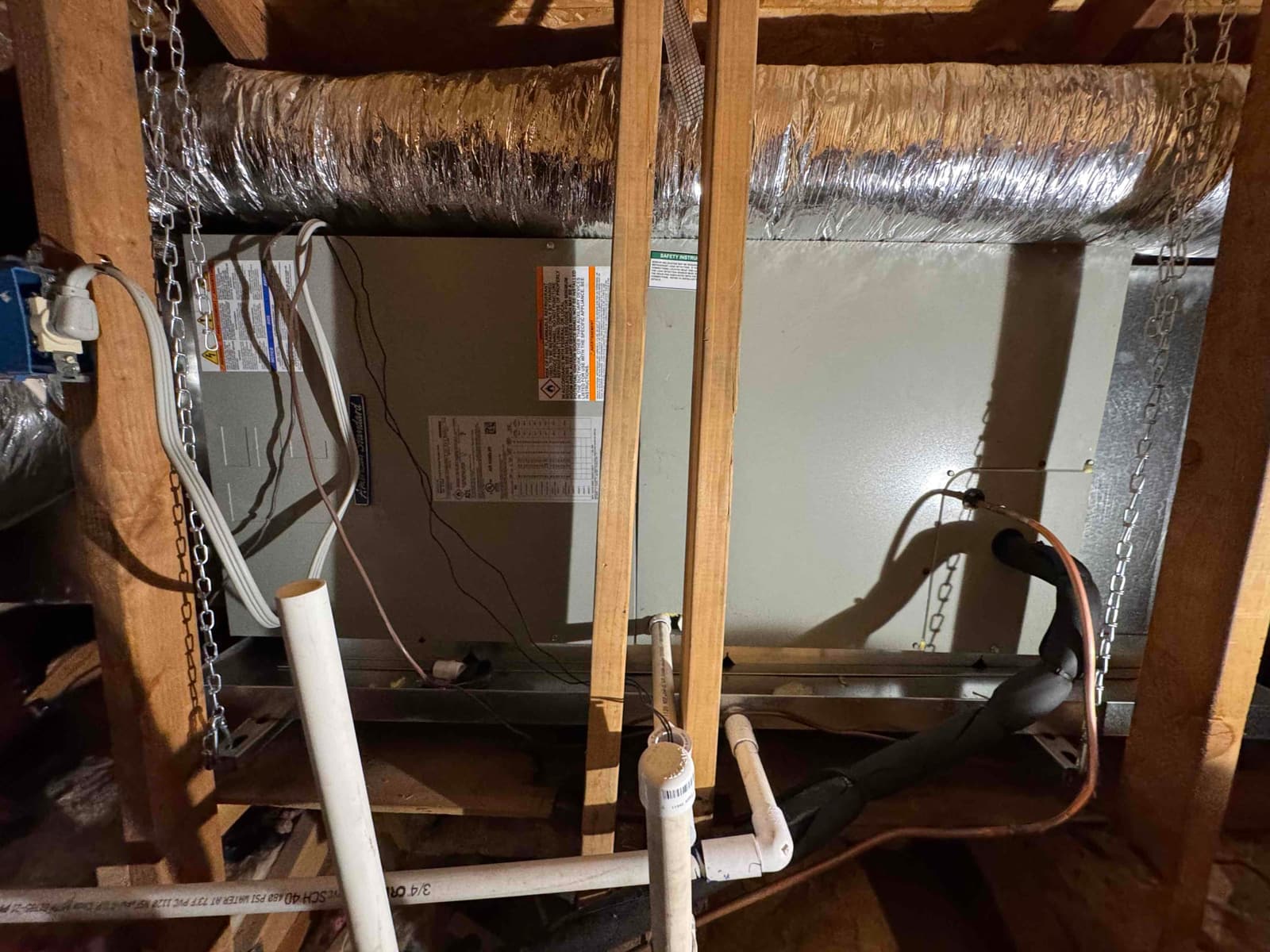 New attic air handler hung with chains, connected to insulated ducts, condensate drain with cleanout, and insulated refrigerant lines.