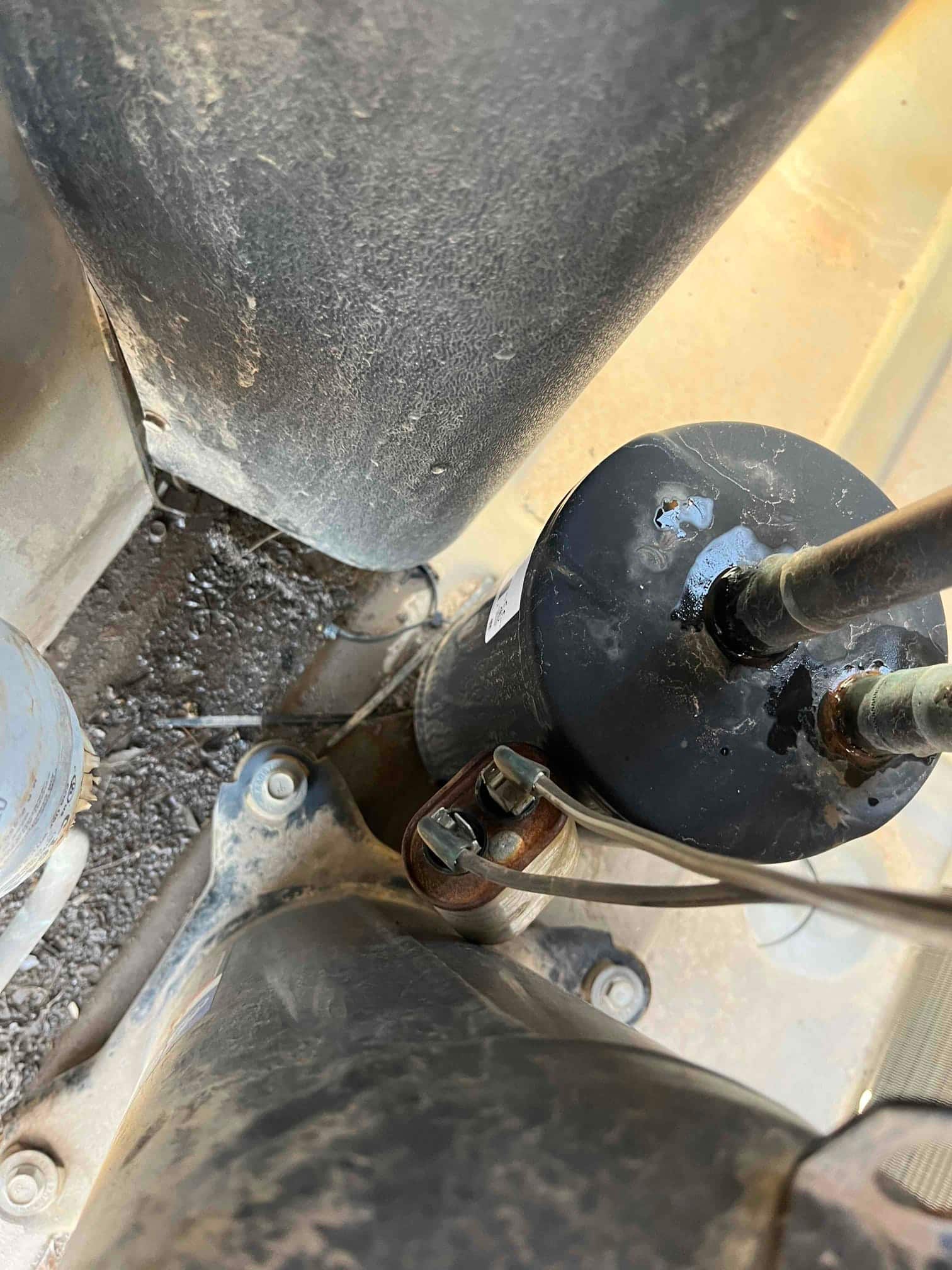 New cylindrical run capacitor installed in the condenser, with wires secured to the terminals and surrounding components visible.