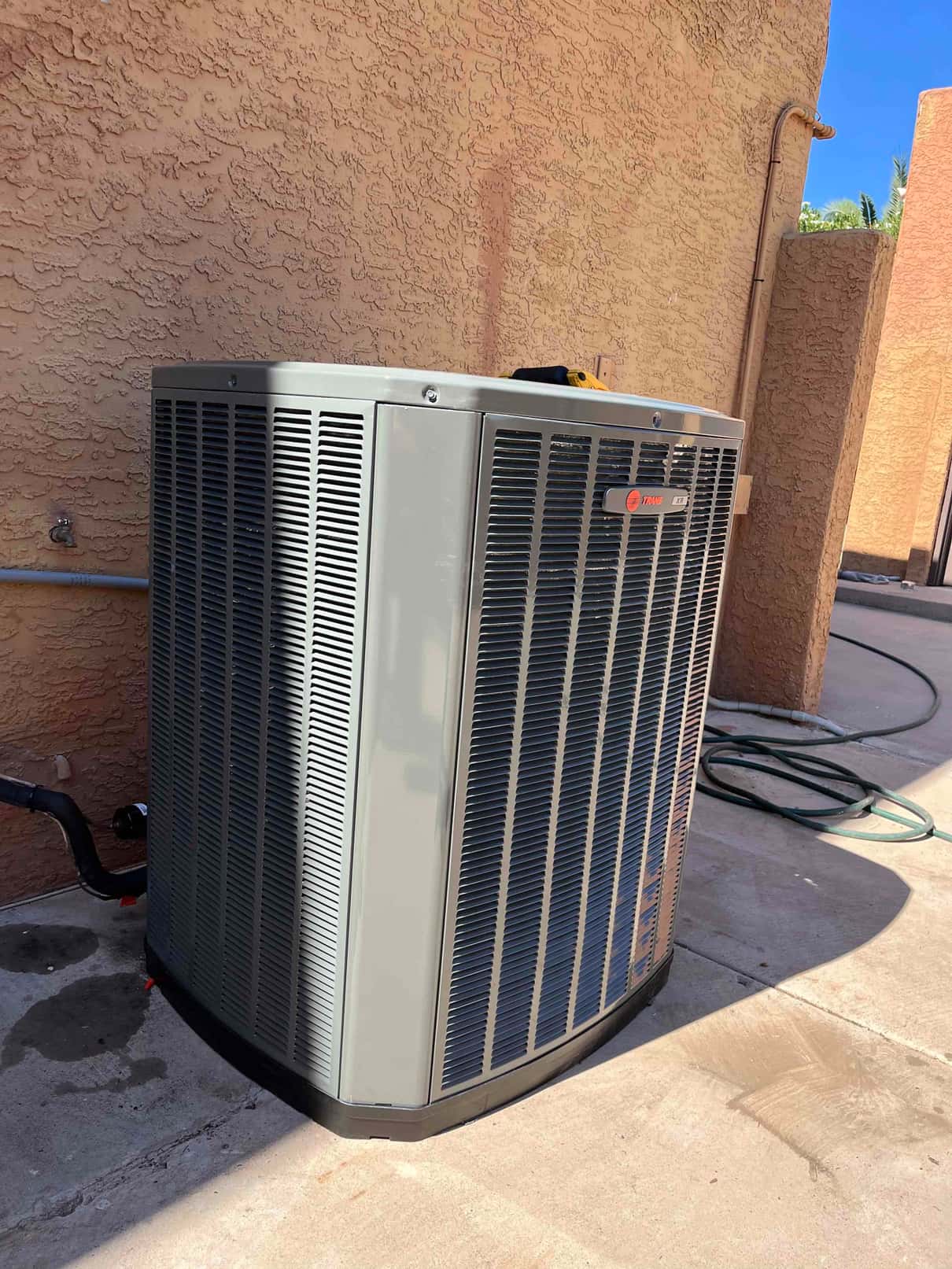 New outdoor heat pump condenser set on a level pad with insulated refrigerant line and wall penetration sealed.