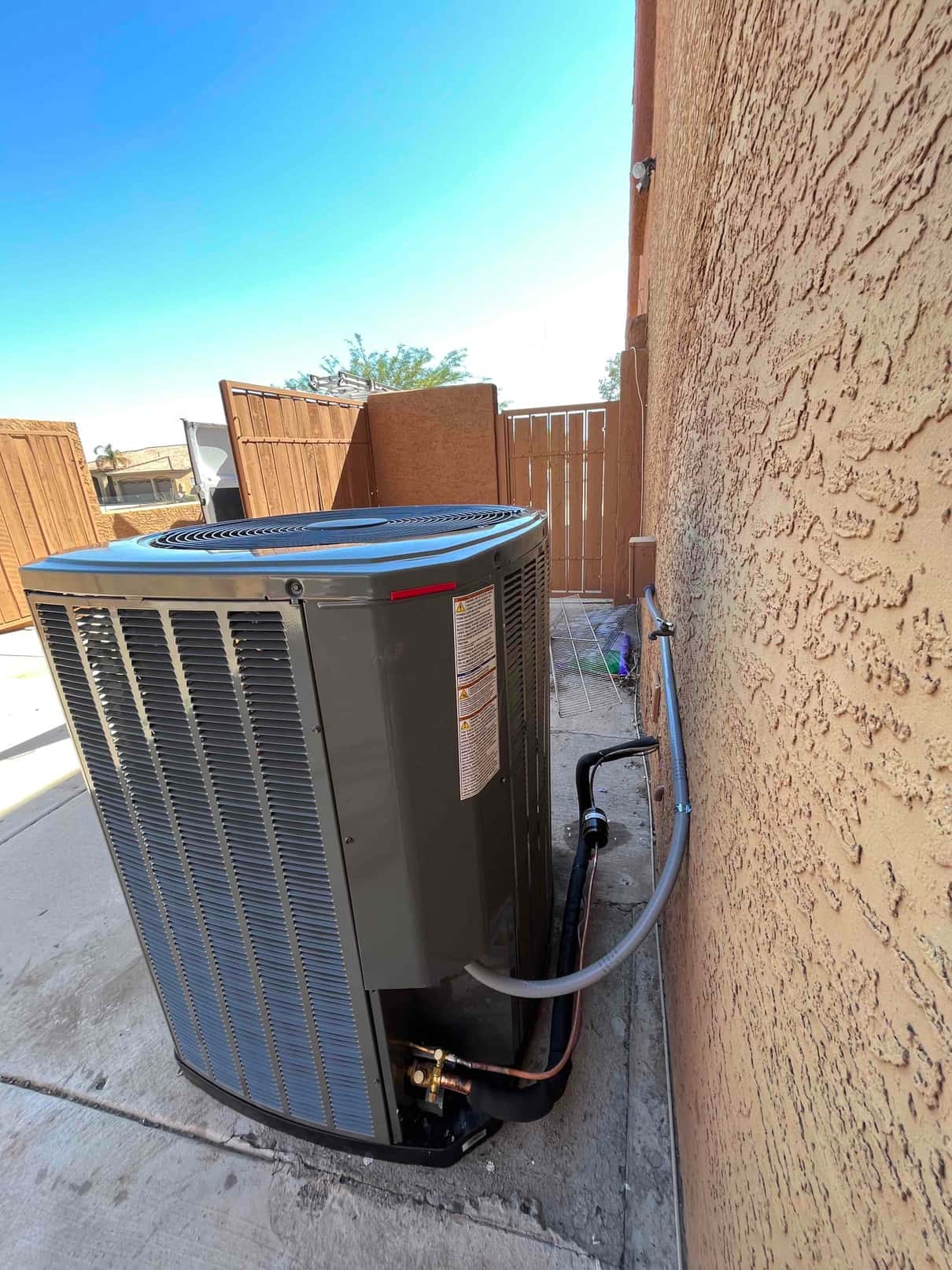 New outdoor heat pump condenser set on a level pad with insulated refrigerant lines and flexible electrical whip routed along the wall.