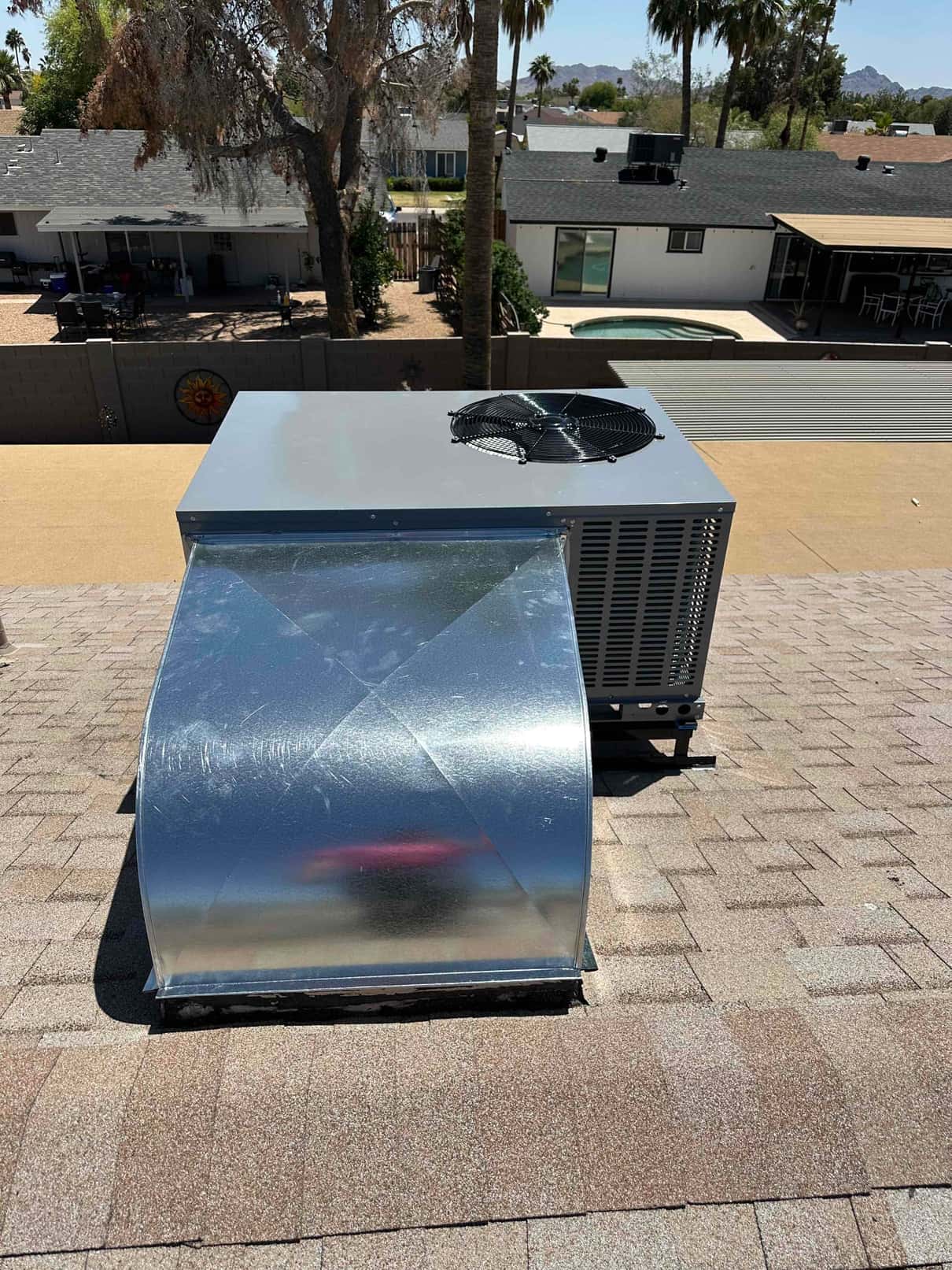 New rooftop package unit installed on shingle roof with sheet metal curb and supply/return duct transition sealed at the base.