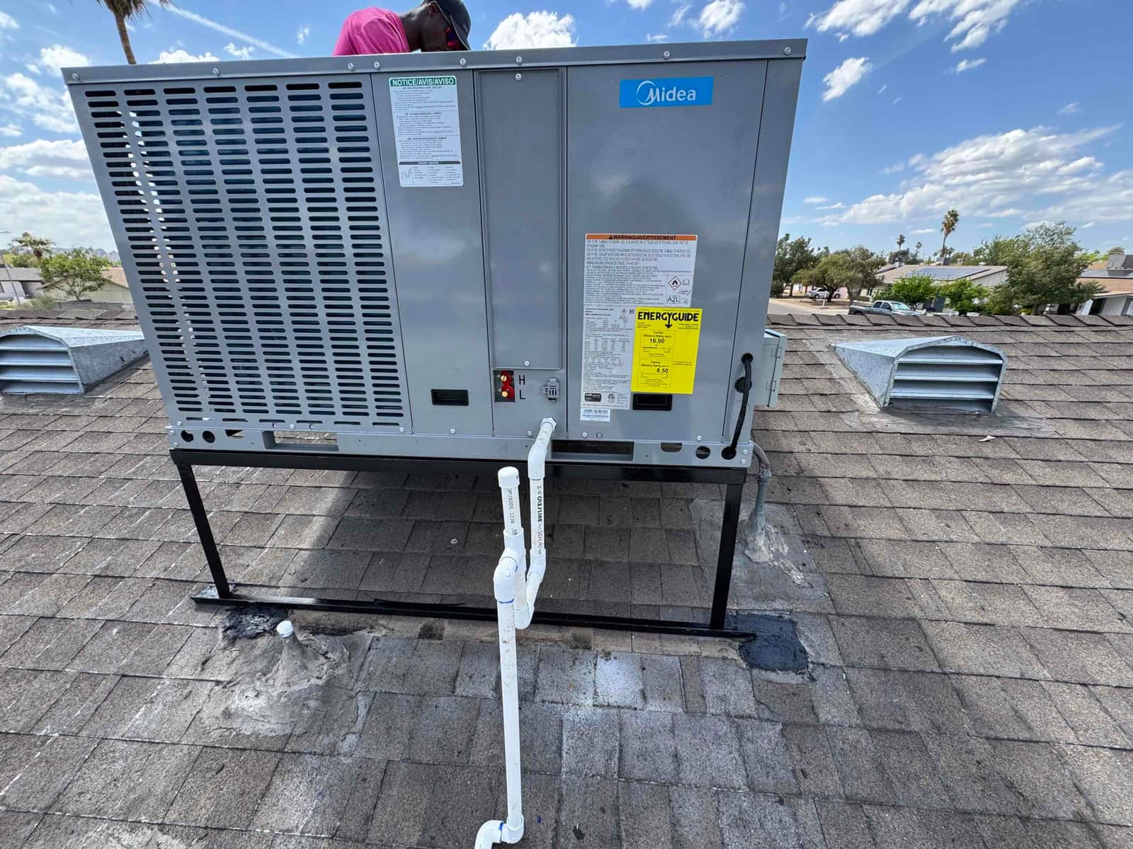 New rooftop package unit mounted on a steel stand with connected condensate drain and roof penetrations sealed.