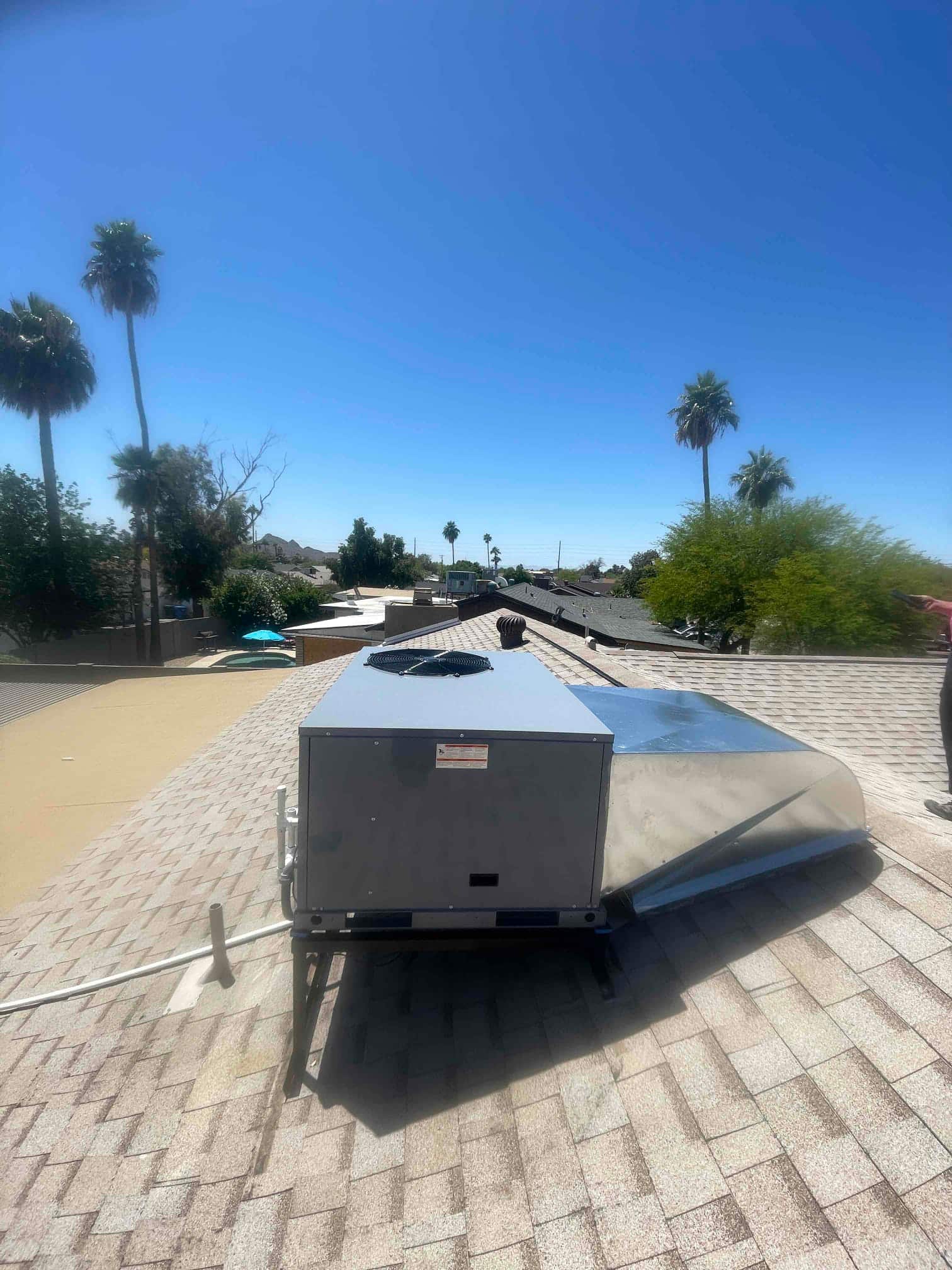 New rooftop package unit set on curb with connected supply/return ductwork and condensate drain routed across shingles.