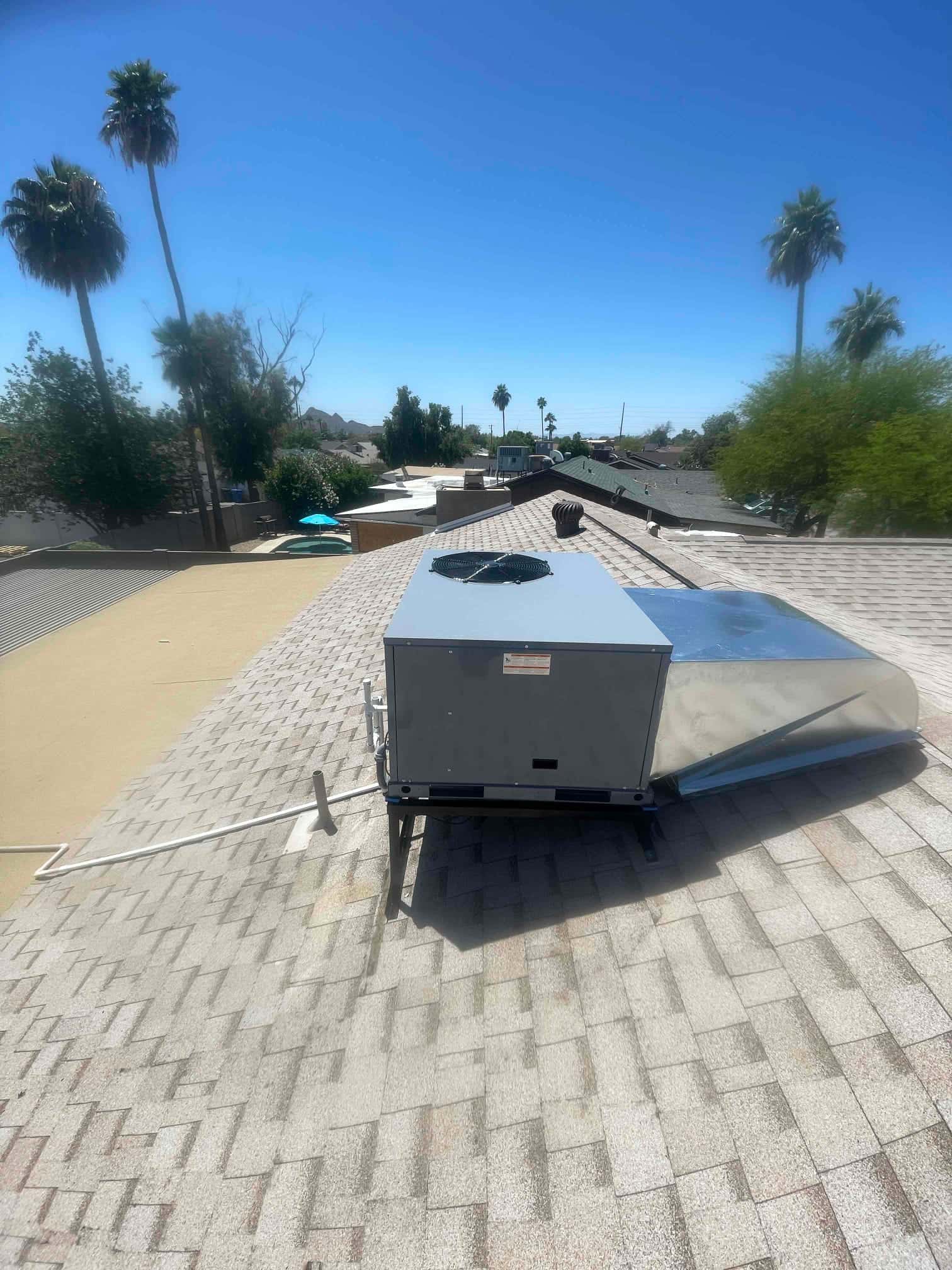 New rooftop package unit set on a stand with attached duct transition and condensate drain routed across the shingles.