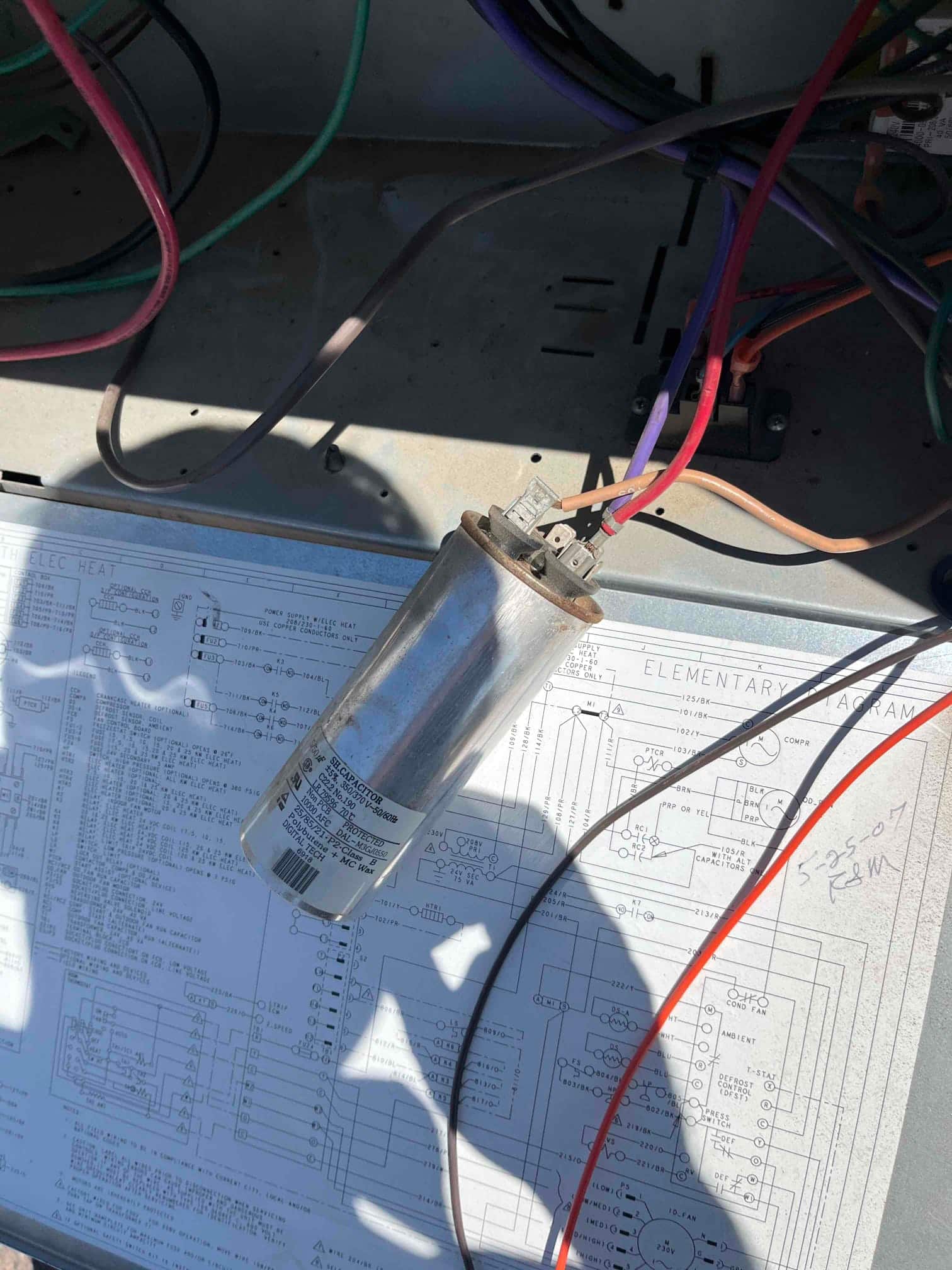 Old turbo run capacitor removed from the condenser panel, showing wiring terminals and printed specification label on the cylinder.