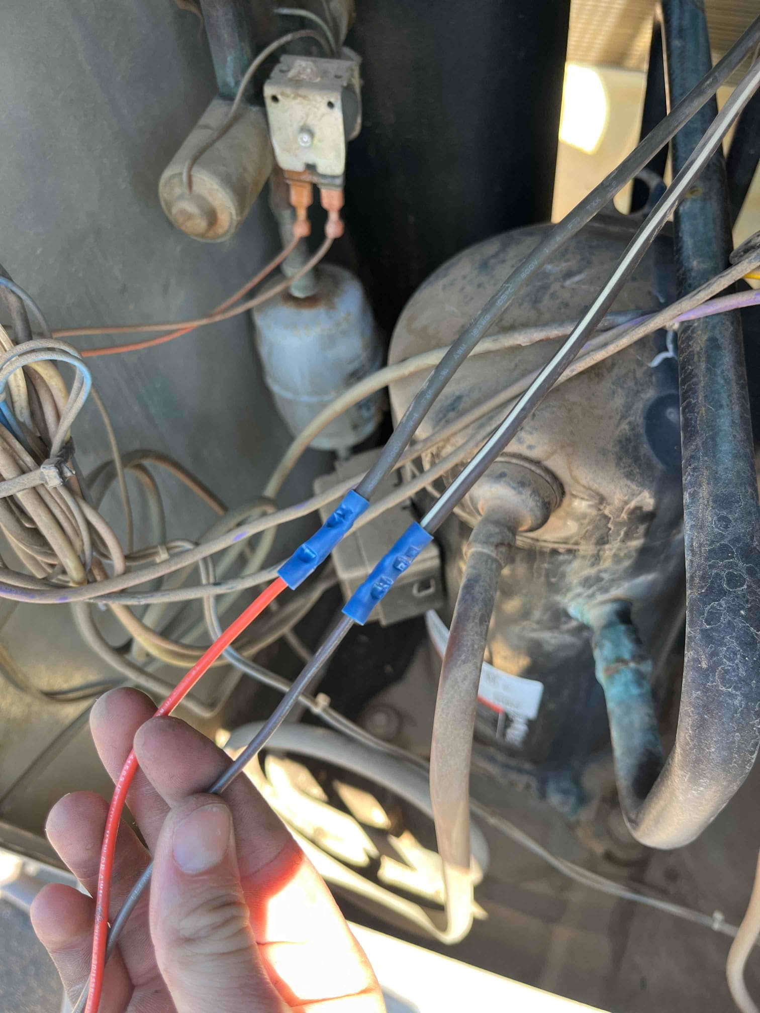 Outdoor condenser compartment showing compressor, installed run capacitor in the background, and re-terminated control wires with blue insulated connectors.