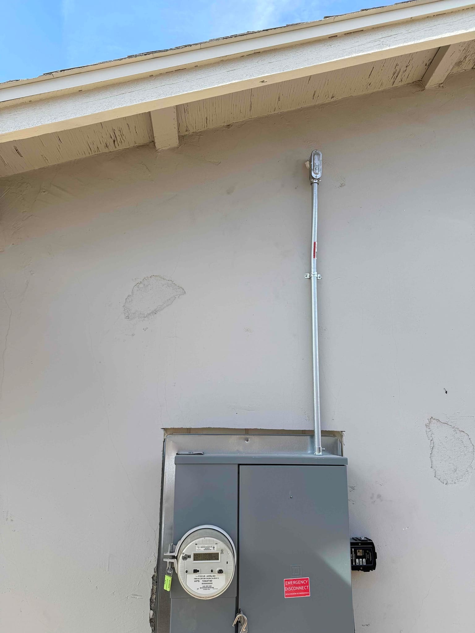Outdoor electrical service panel with meter and new conduit riser installed on the exterior wall near the roof eave.