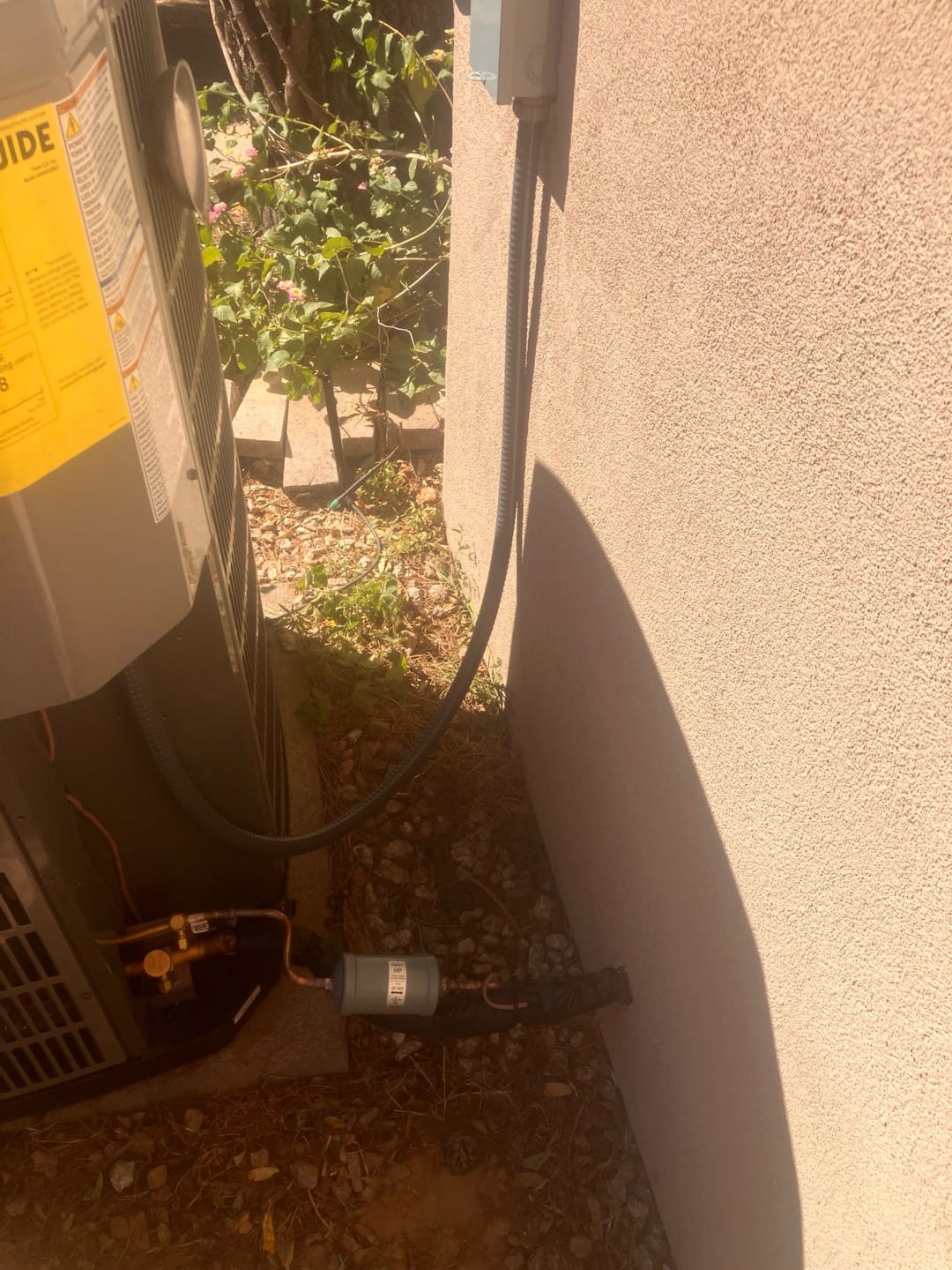 Outdoor heat pump condenser set beside the house with new electrical disconnect and insulated refrigerant line set routed to the wall.