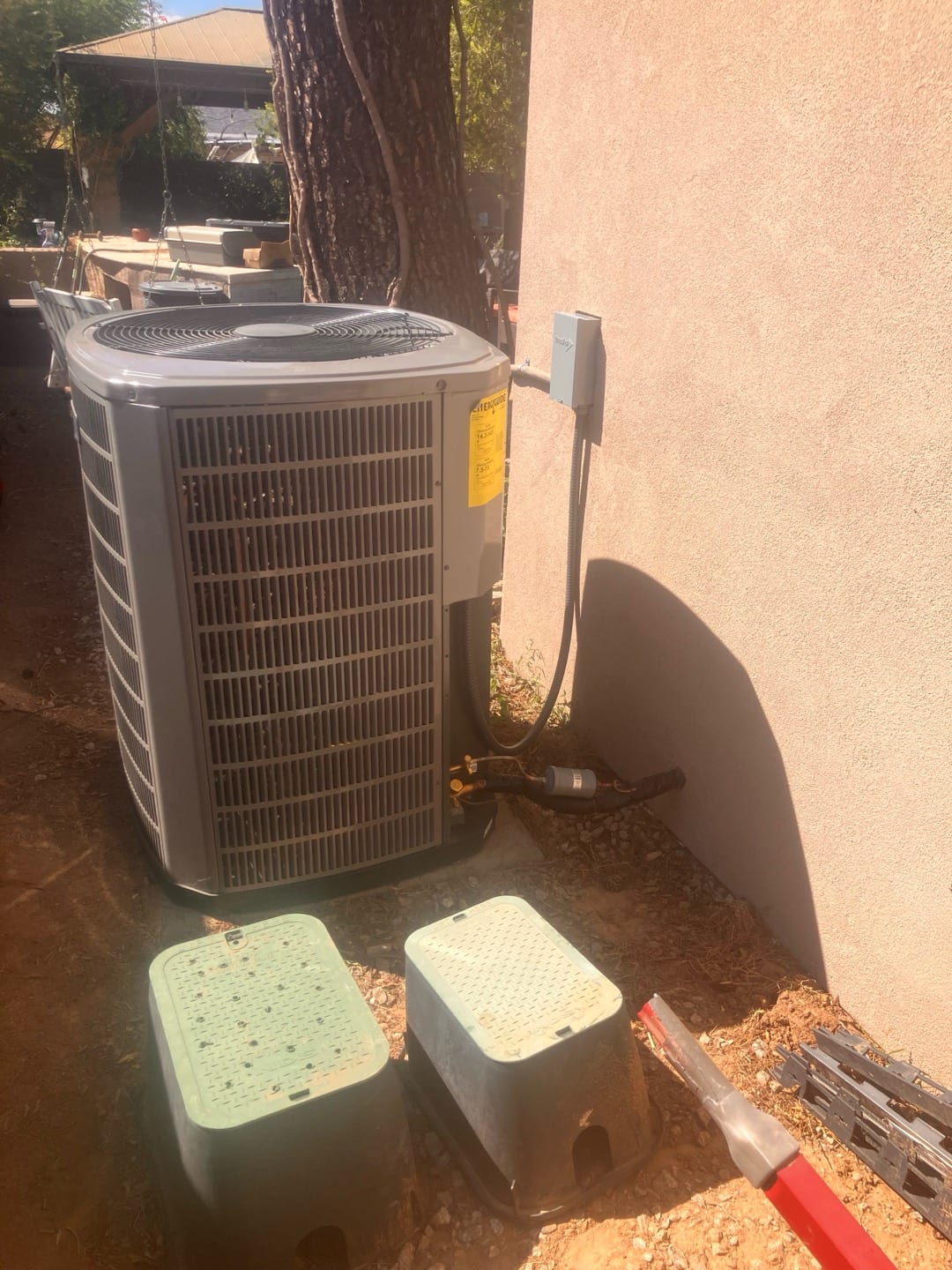 Outdoor heat pump condenser set on a pad with insulated refrigerant lines and weatherproof disconnect mounted on the wall.