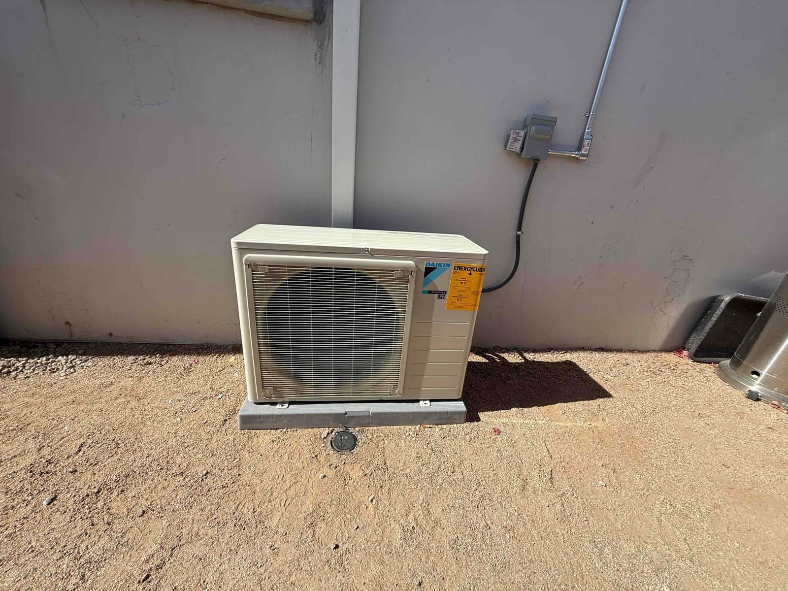 Outdoor mini-split condenser set on a level pad with electrical disconnect installed and conduit neatly routed along the wall.
