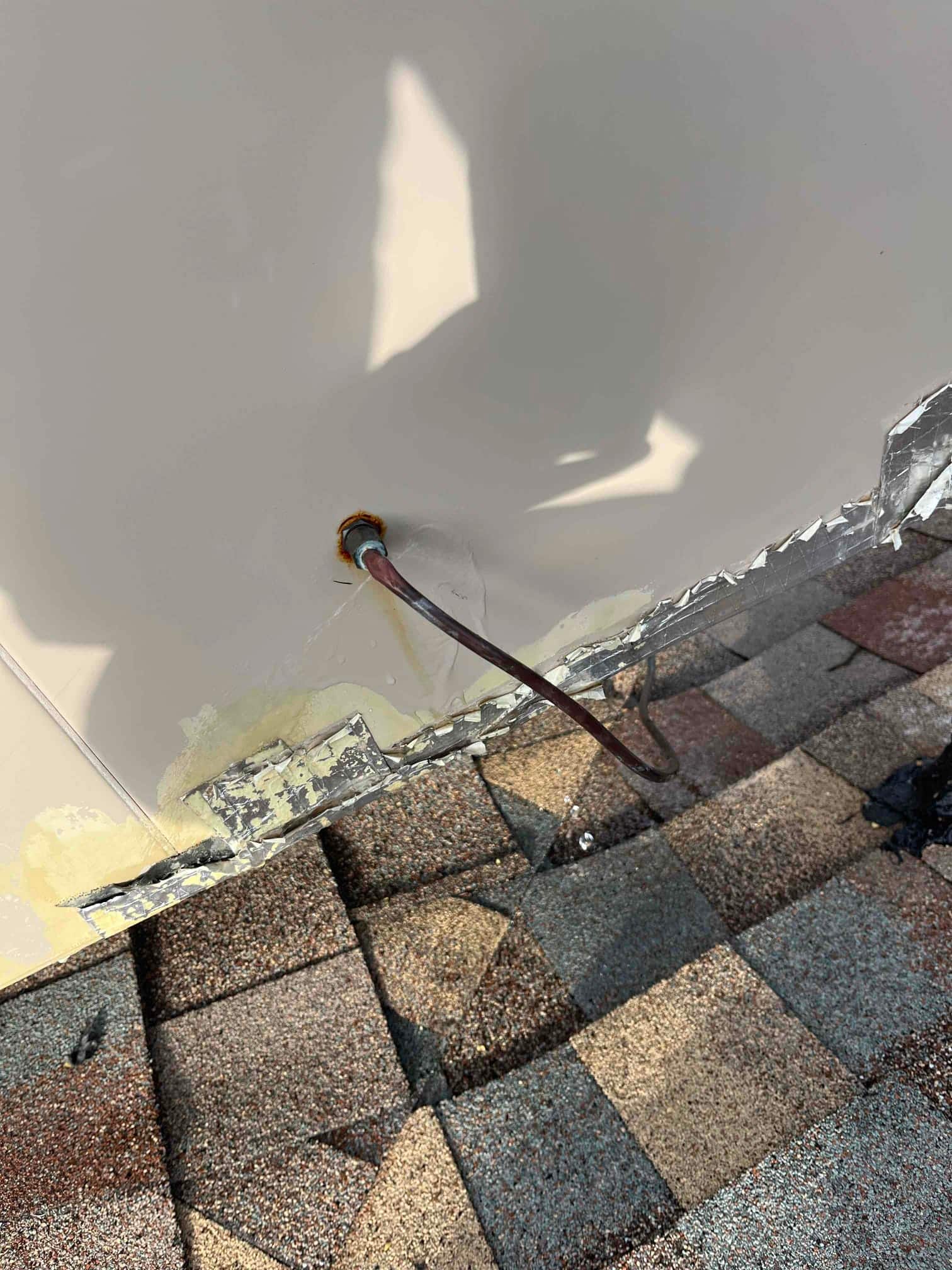 Roof-mounted HVAC cabinet penetration with a single copper tube exiting a deteriorated wall opening above asphalt shingles.