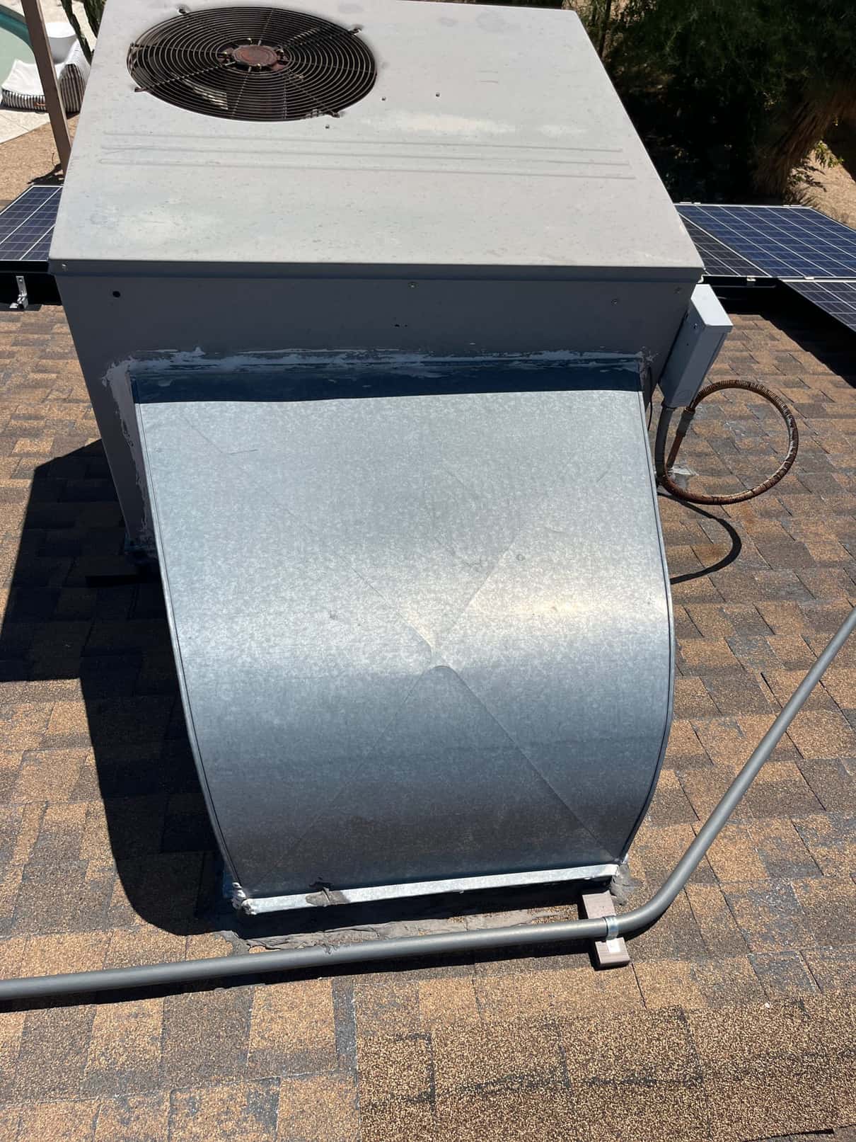 Rooftop air conditioning package unit with galvanized return duct and electrical conduit visible on the shingle roof.