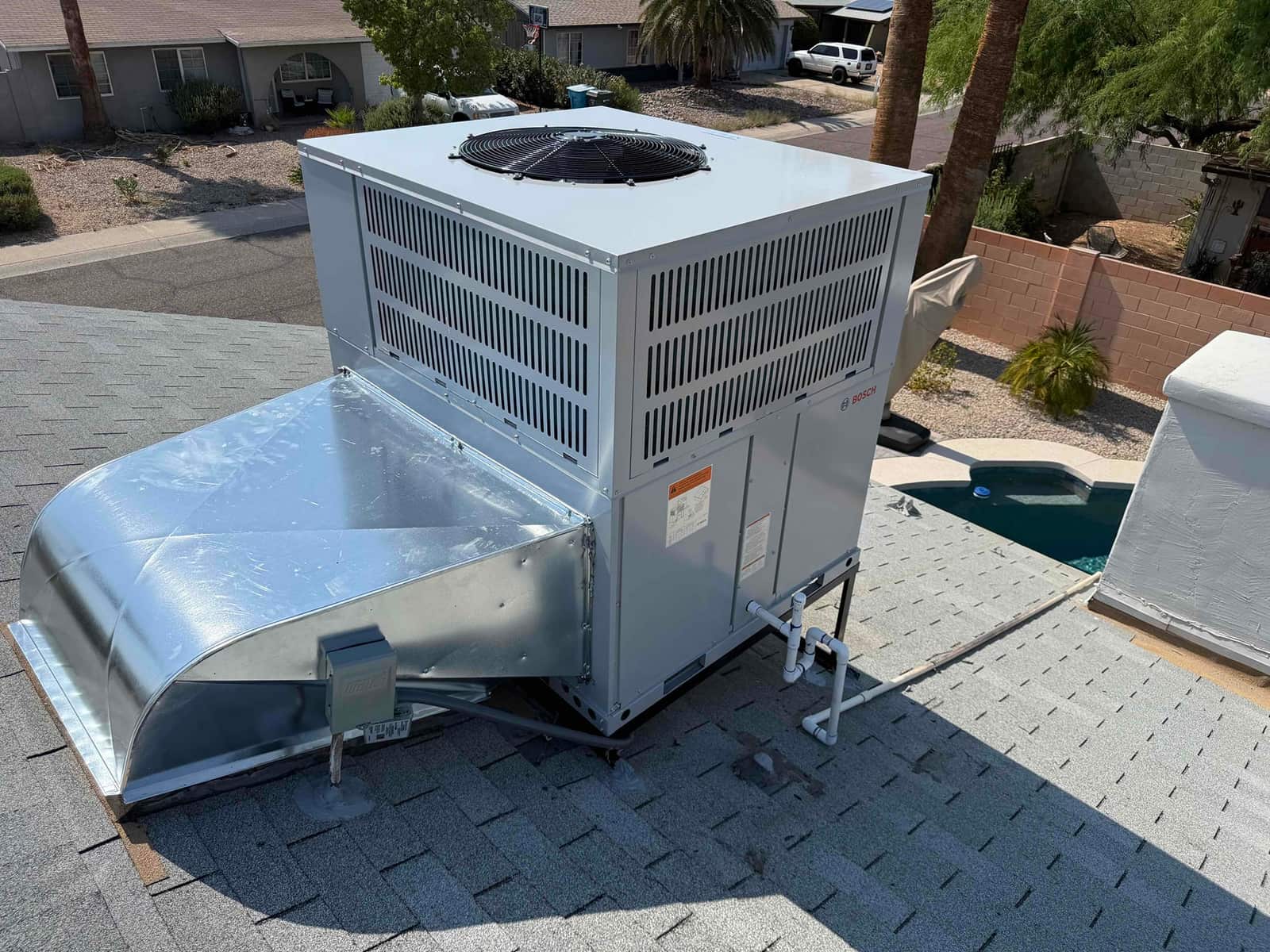 Rooftop packaged HVAC unit newly installed with metal curb adapter, sealed duct transition, electrical disconnect, and condensate drain piping.