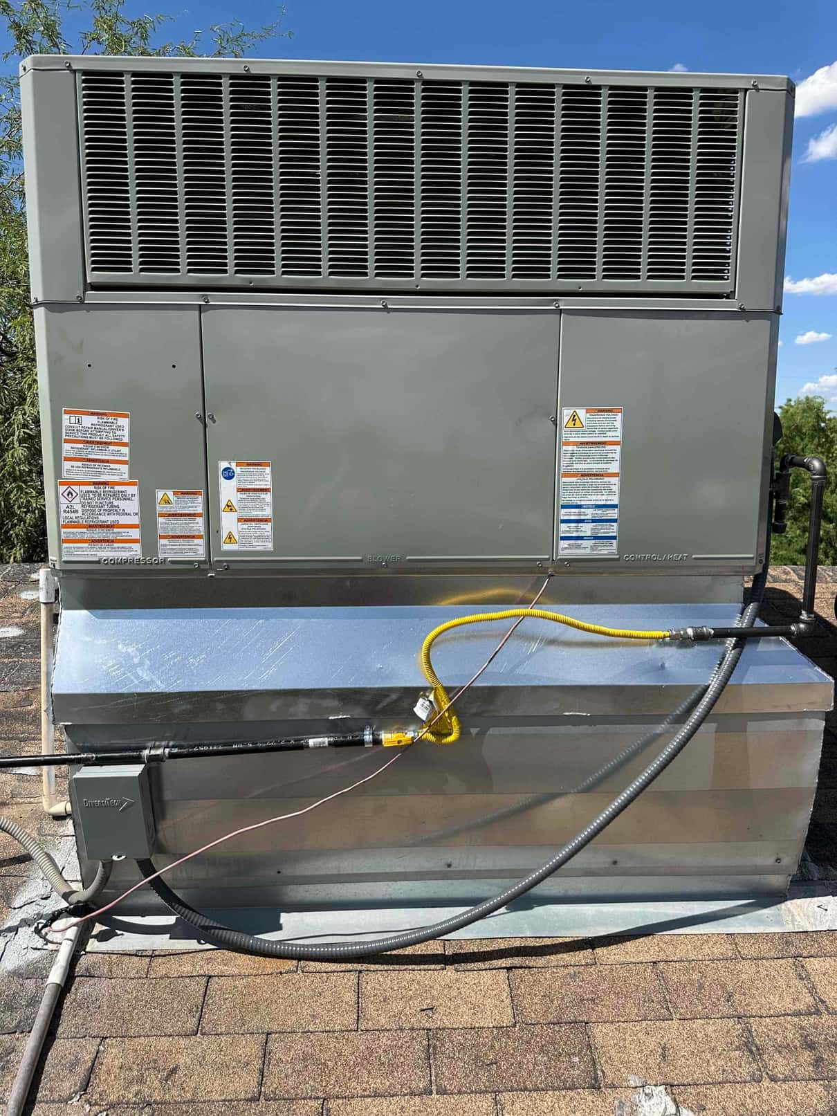 Rooftop packaged HVAC unit newly set on curb with connected gas line, electrical conduit, and sealed roof penetration.