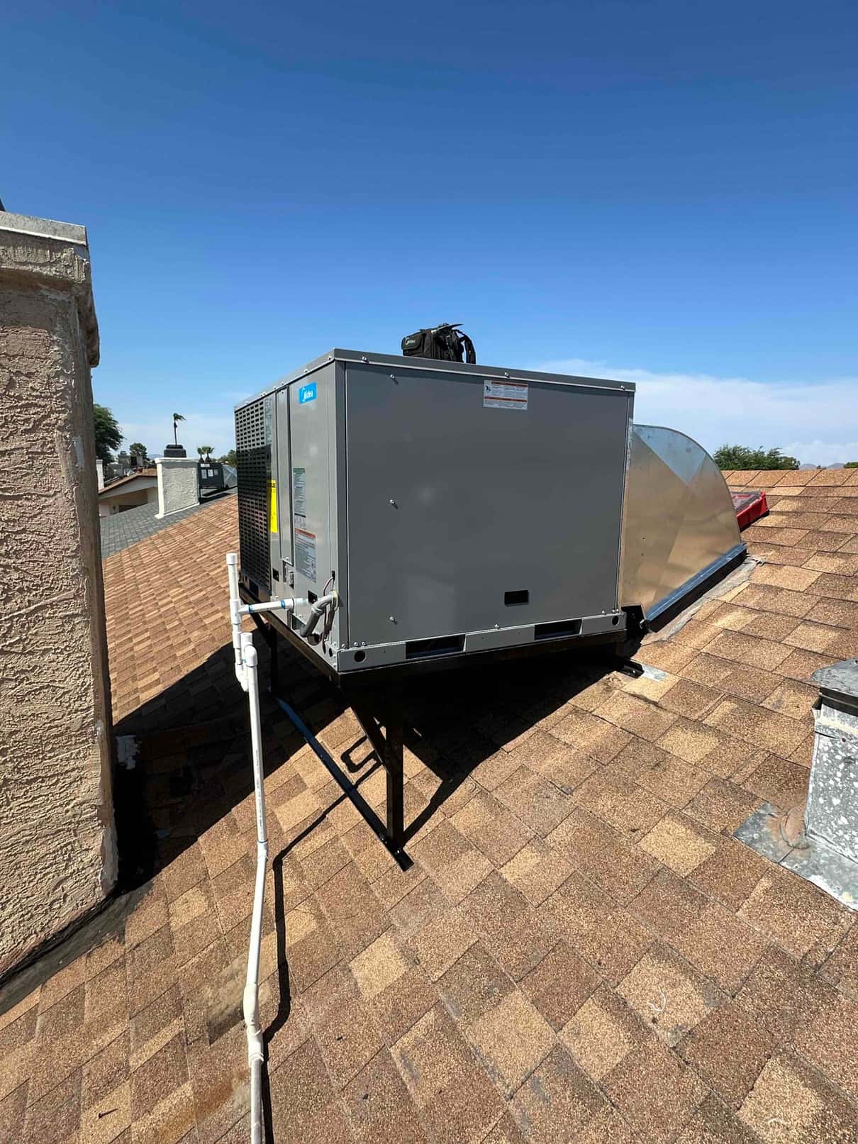 Rooftop packaged HVAC unit set on a metal stand with new condensate drain piping and sheet-metal supply/return transition.